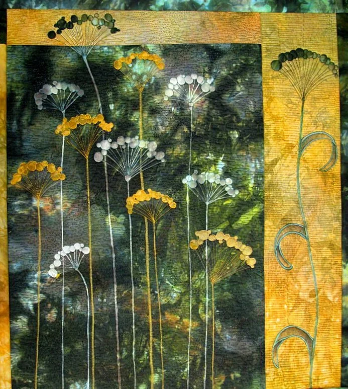 Colorful abstract fabric art depicting tall flowering plants with circular blooms and a textured background, framed by a yellow border.