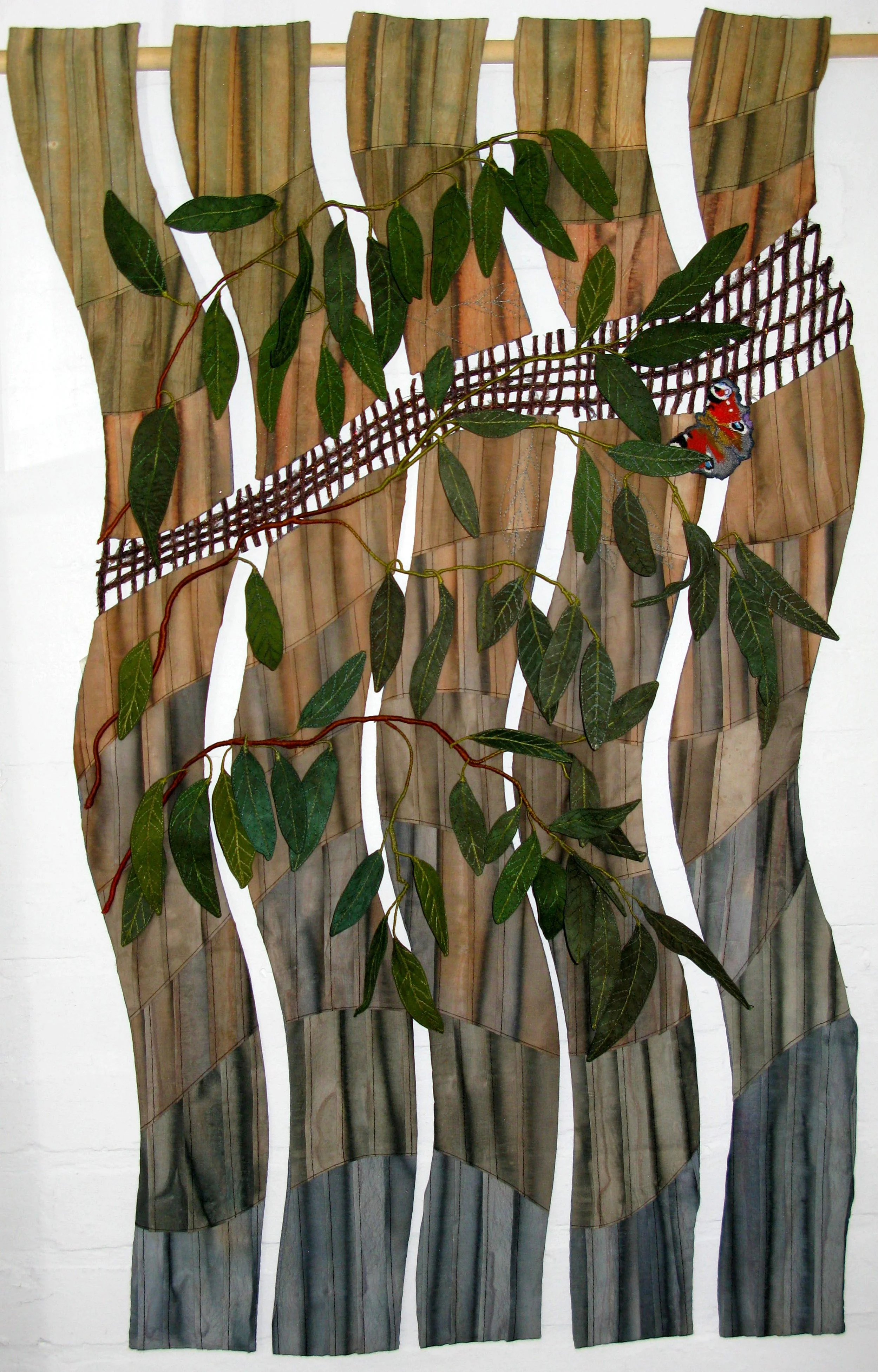 Textile wall art featuring vertical wavy panels in earthy tones, with green leaves and a small colorful bird design.