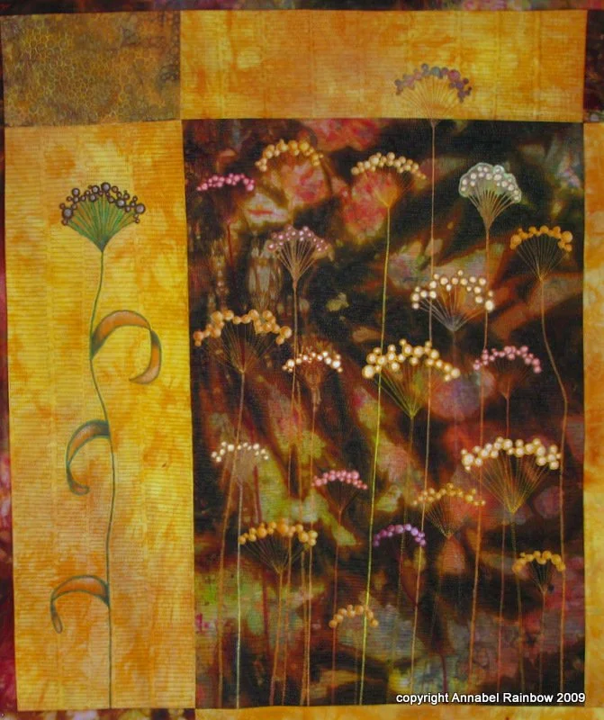 Art quilt featuring abstract floral designs on a textured yellow and brown background.