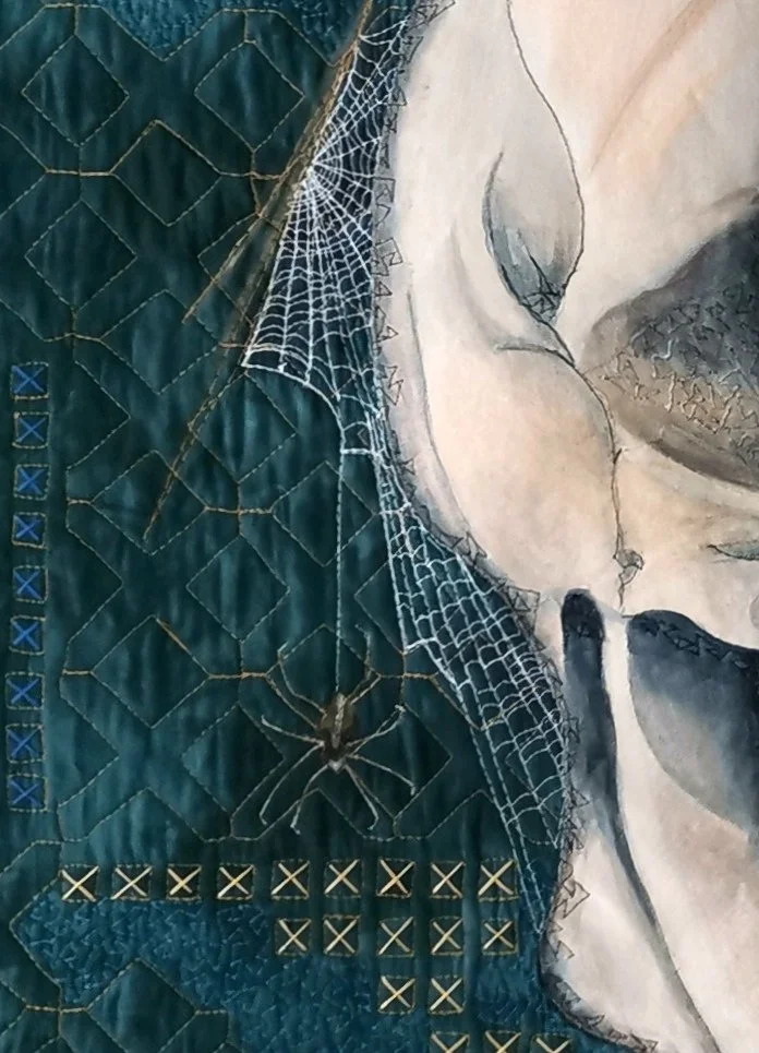 Artistic quilt with a skull, spider web, and spider on a textured blue background with embroidery.