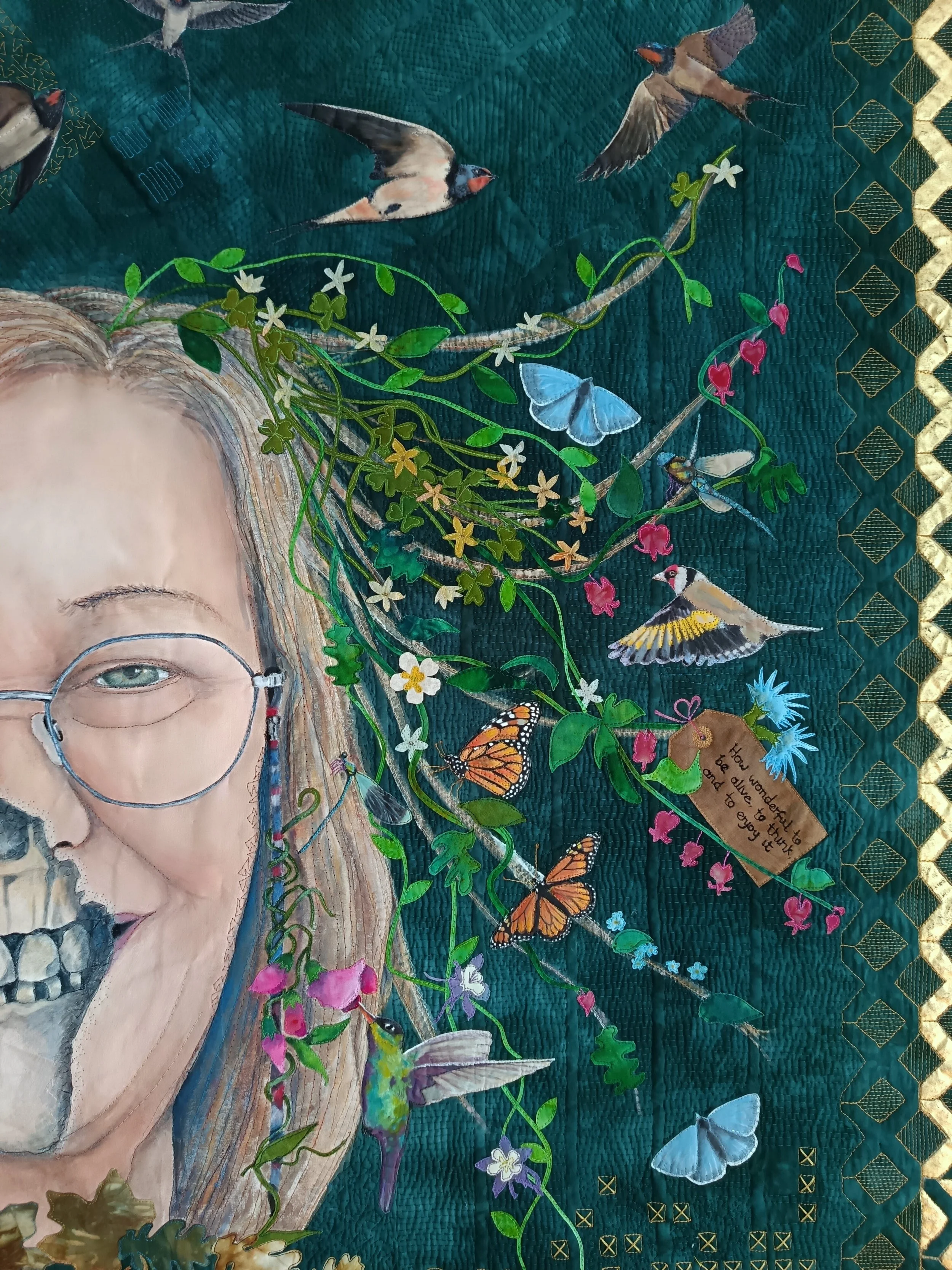 Artwork depicting a woman's face, partially transformed into a skull, surrounded by birds, butterflies, and flowers against a textured green background. A handwritten note is attached to a branch.