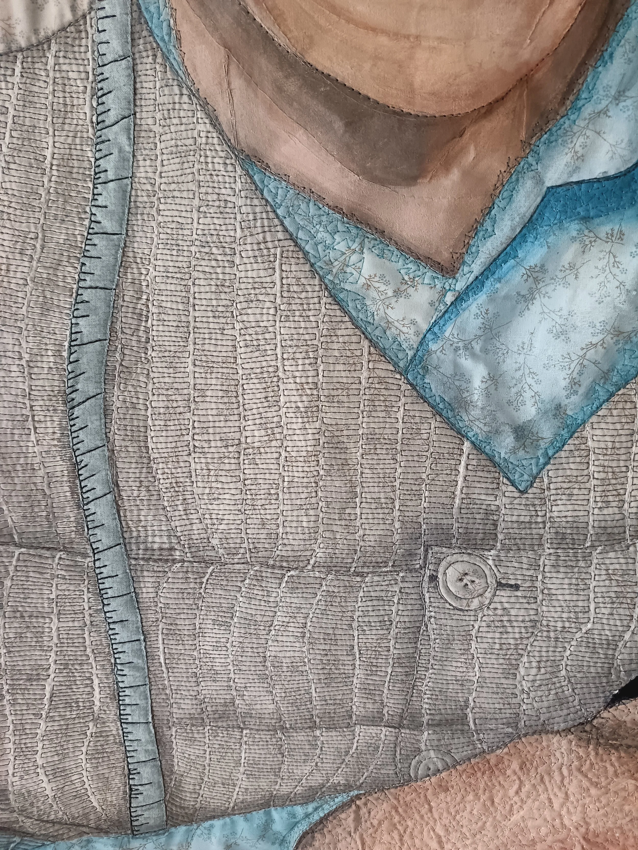 Close-up of textile art featuring a detailed quilted vest with a button, intricate stitching, and blue patterned fabric detail, resembling a shirt collar and lapel.