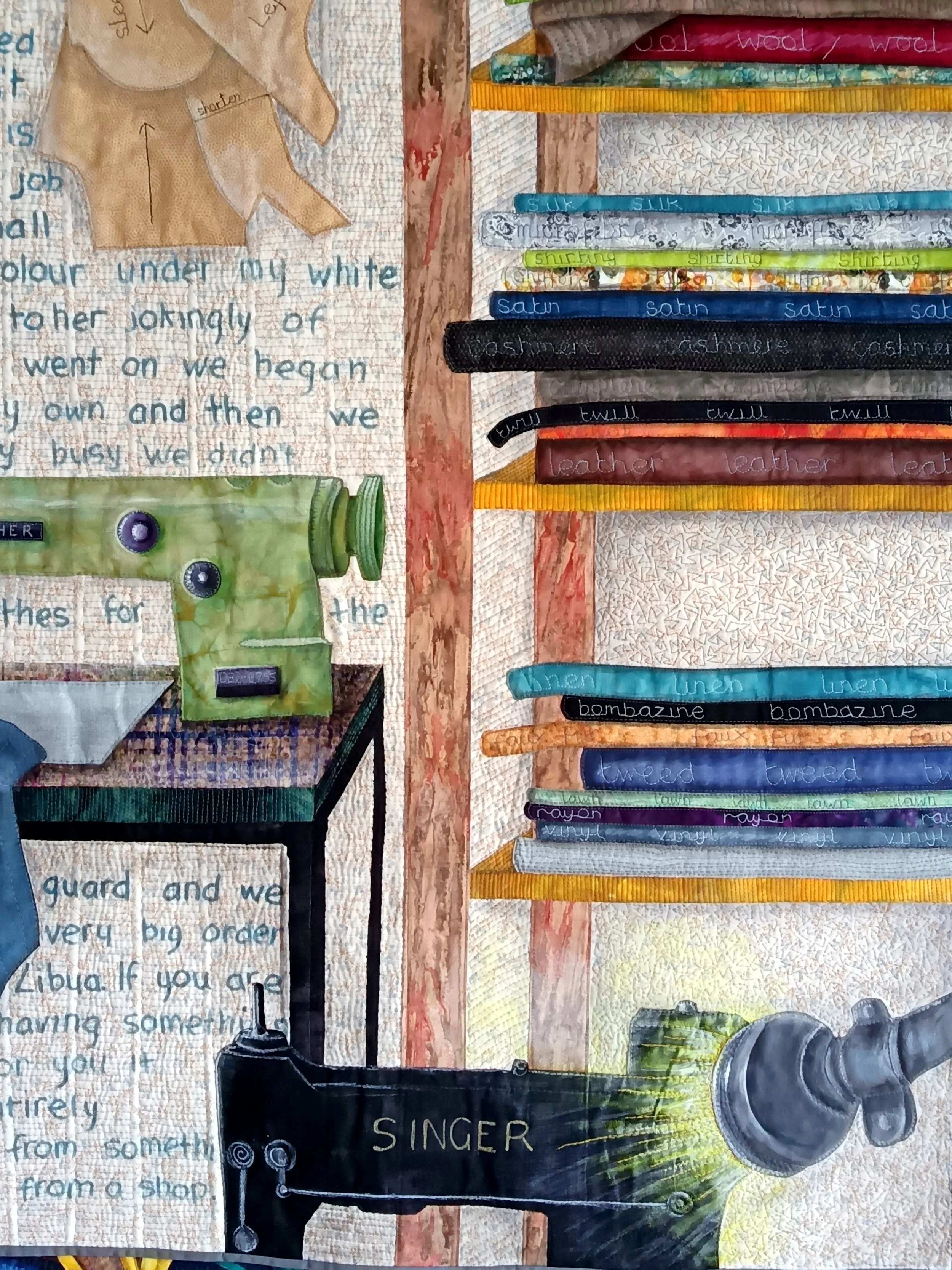 Quilted artwork depicting a sewing scene with a Singer sewing machine, fabric shelves labeled with various textiles like satin and wool, pattern pieces, and text background. Features vibrant colors and detailed stitching.