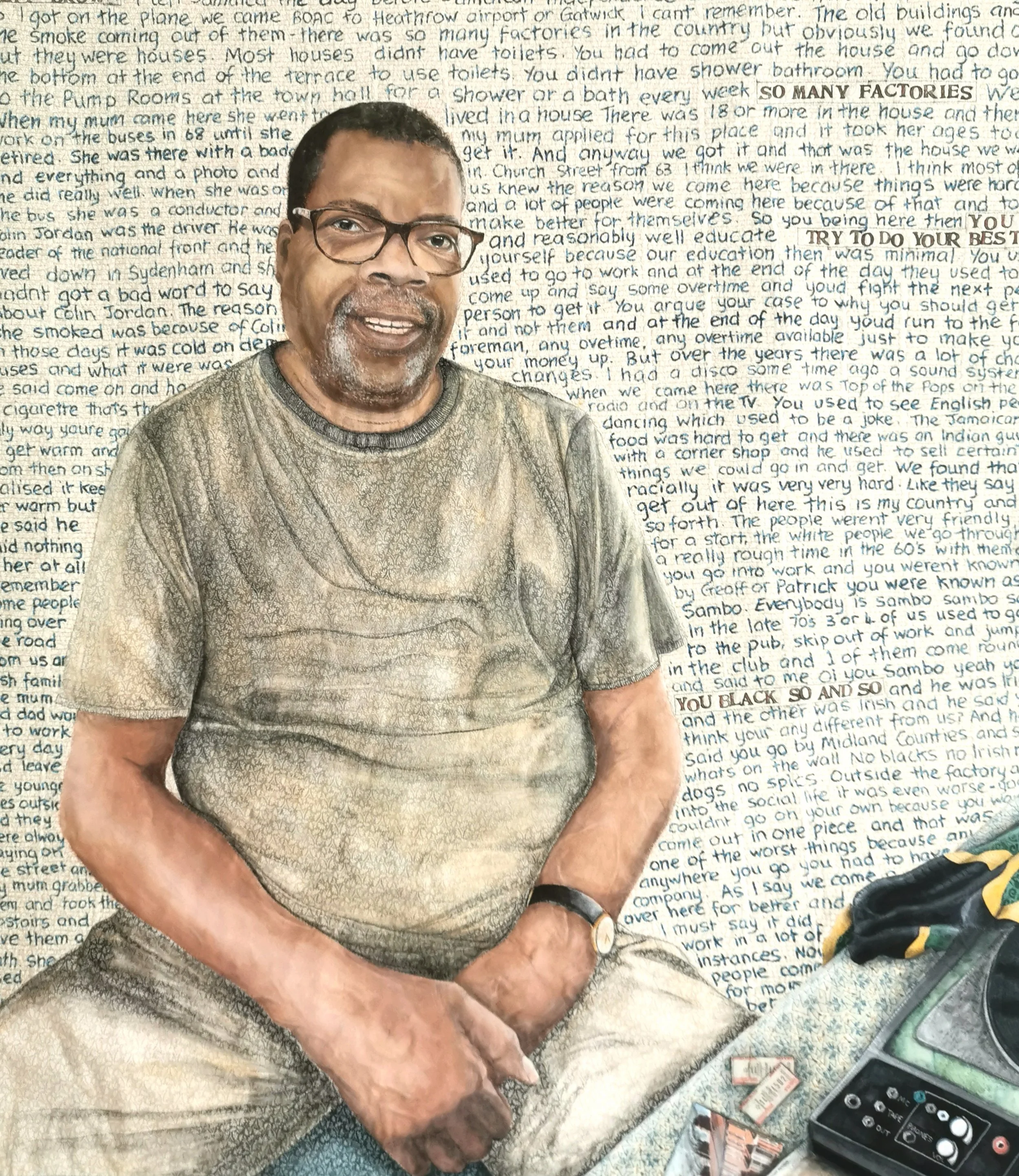 Portrait of a man sitting against a background filled with text. He has glasses, a short haircut, and is wearing a watch and casual clothing. On a nearby surface, there are a radio and several small objects. The text behind him appears to be handwritten and covers the entire background.