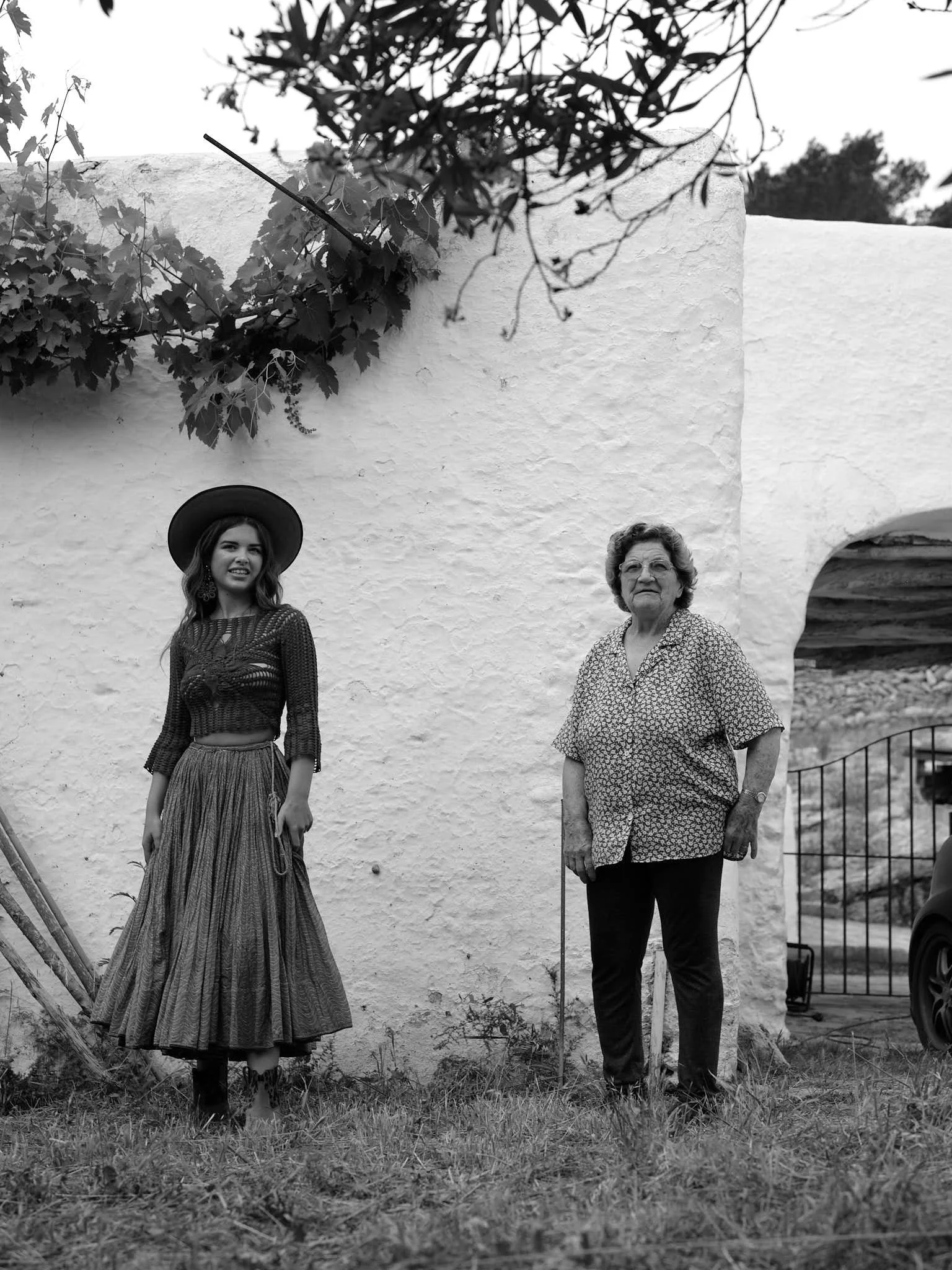 A black and white photo of two women standing in front of a textured white wall belonging to a traditional Ibizan home, heritage and contemporary storytelling.