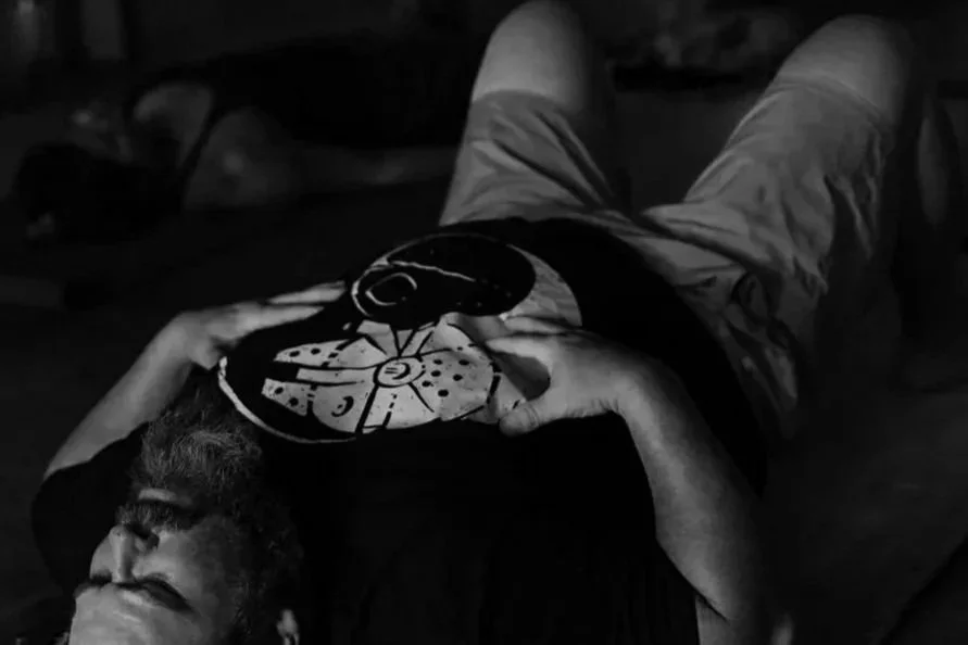 A person lying down, with their head turned to the side and one arm resting on their chest, wearing a T-shirt with a design of a pizza slice and a black circle