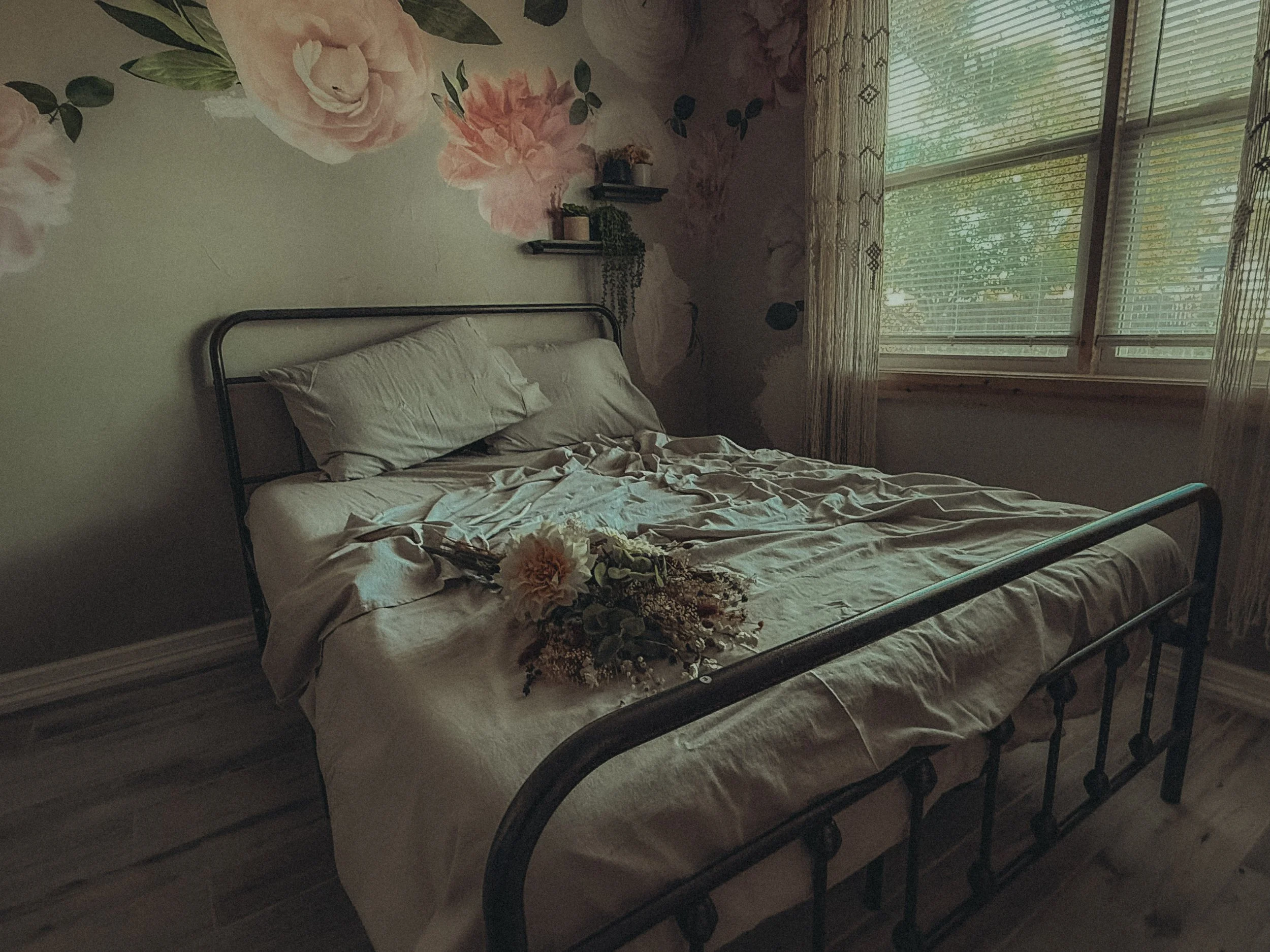 A bedroom with a bed, floral wall art, and window with blinds.