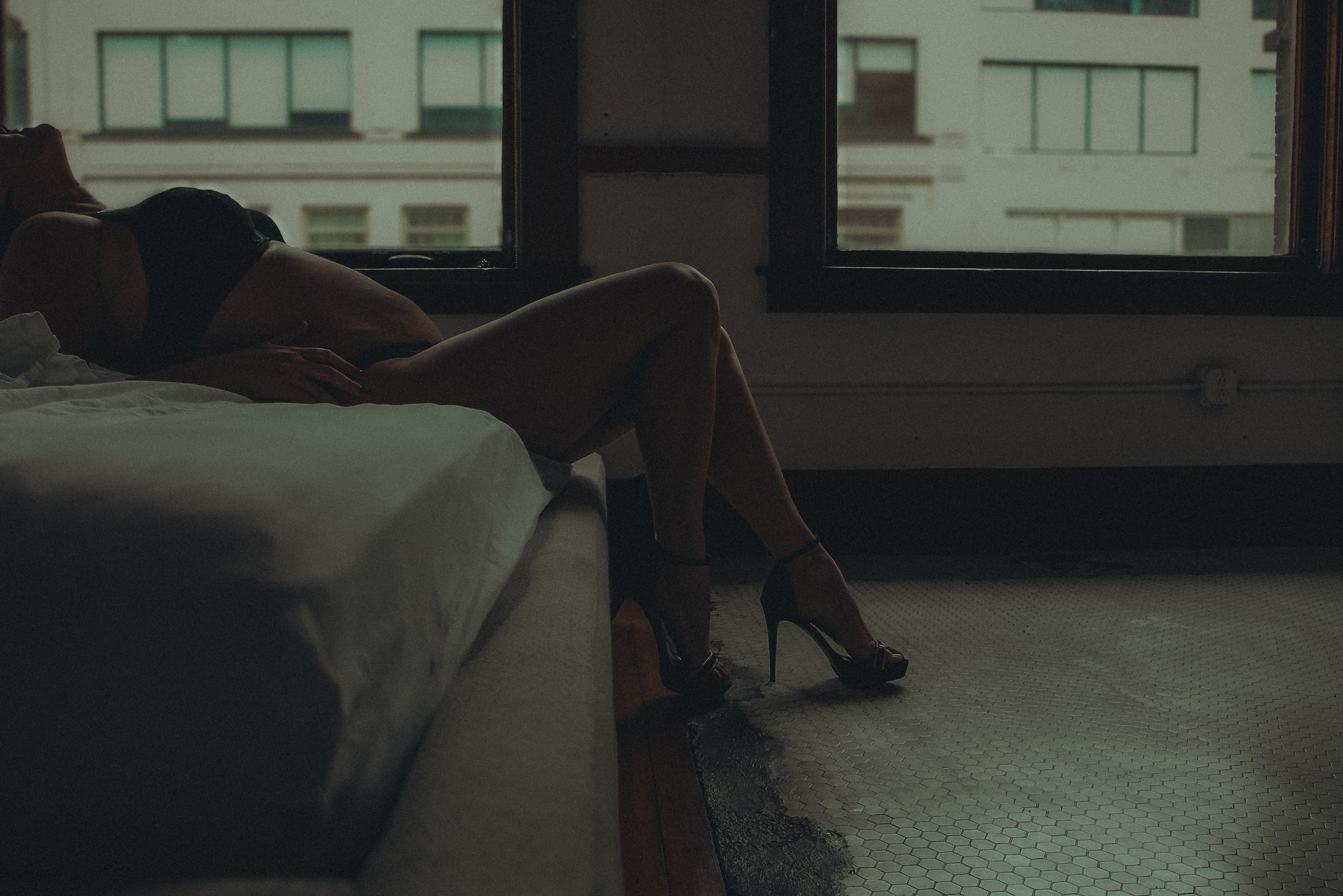 Silhouette of a woman lying on a bed in front of a window, with city buildings visible outside.