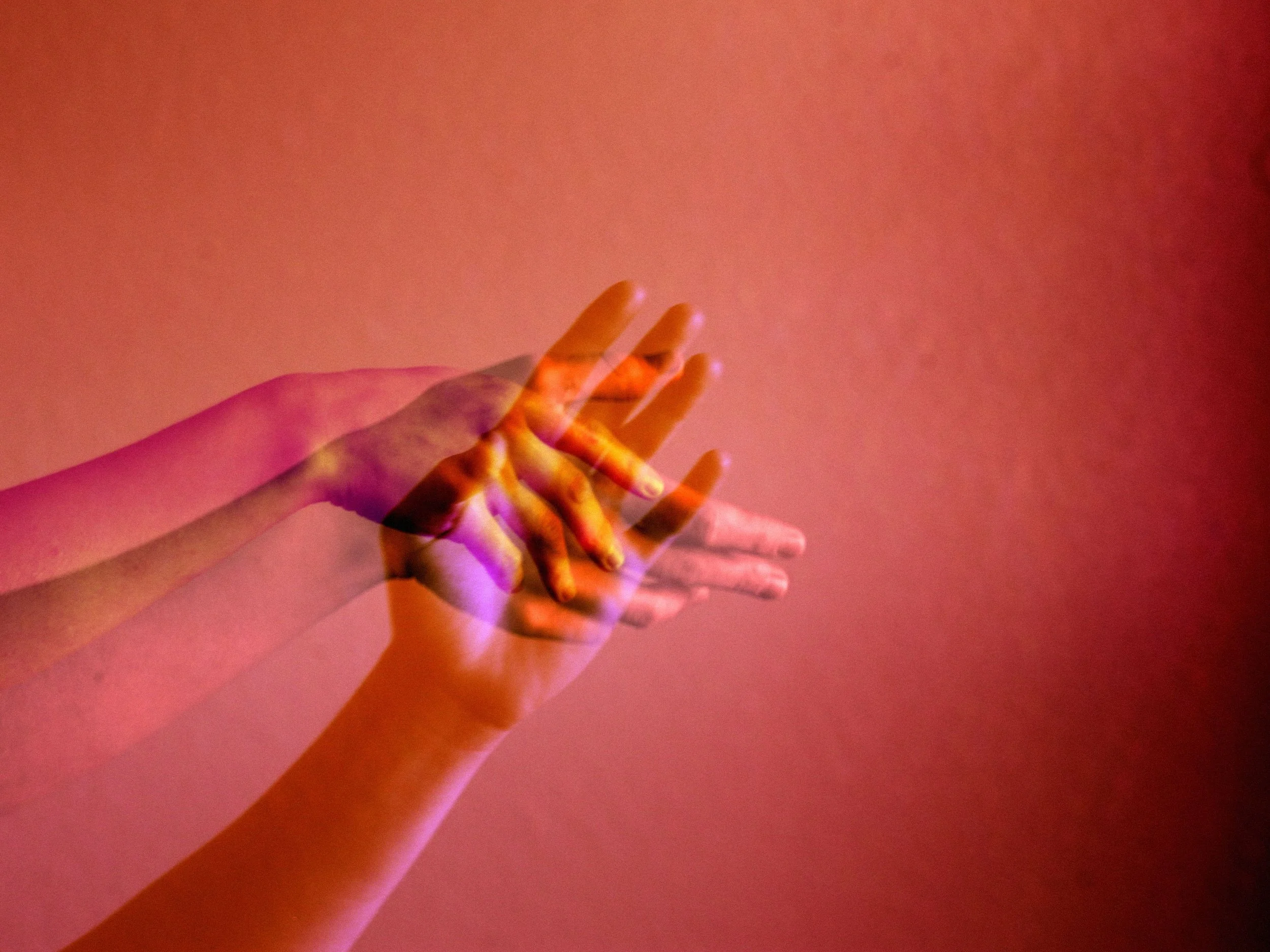 Multiple blurred hands reaching or overlapping over a pinkish-orange background.