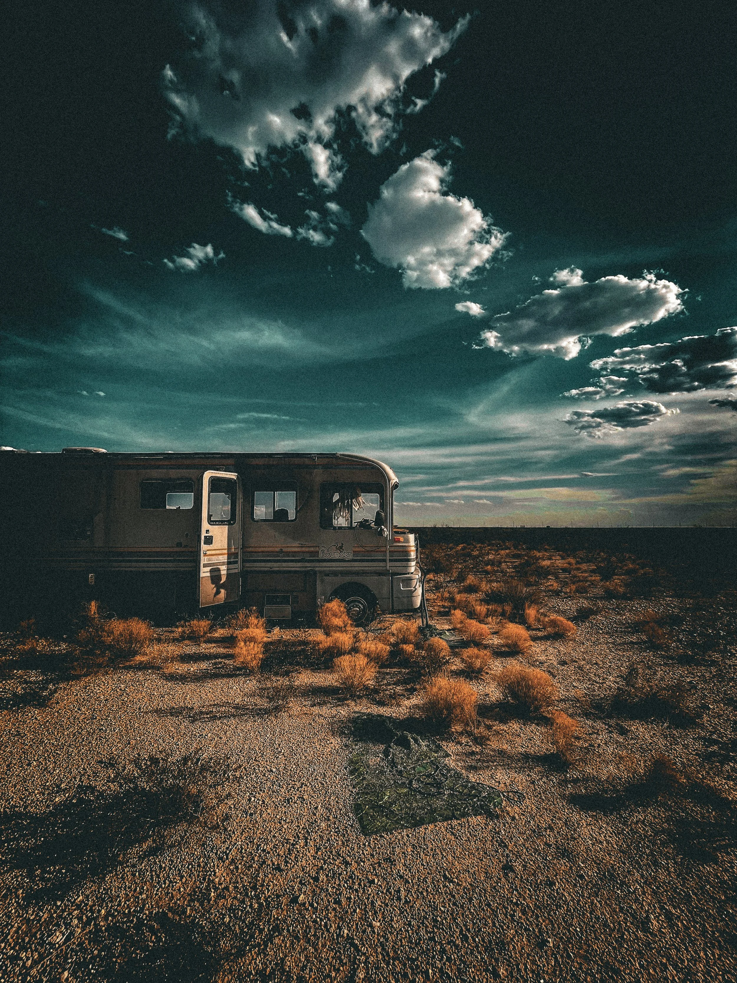 A camper van parked in a desert landscape under a dramatic sky with dark clouds
