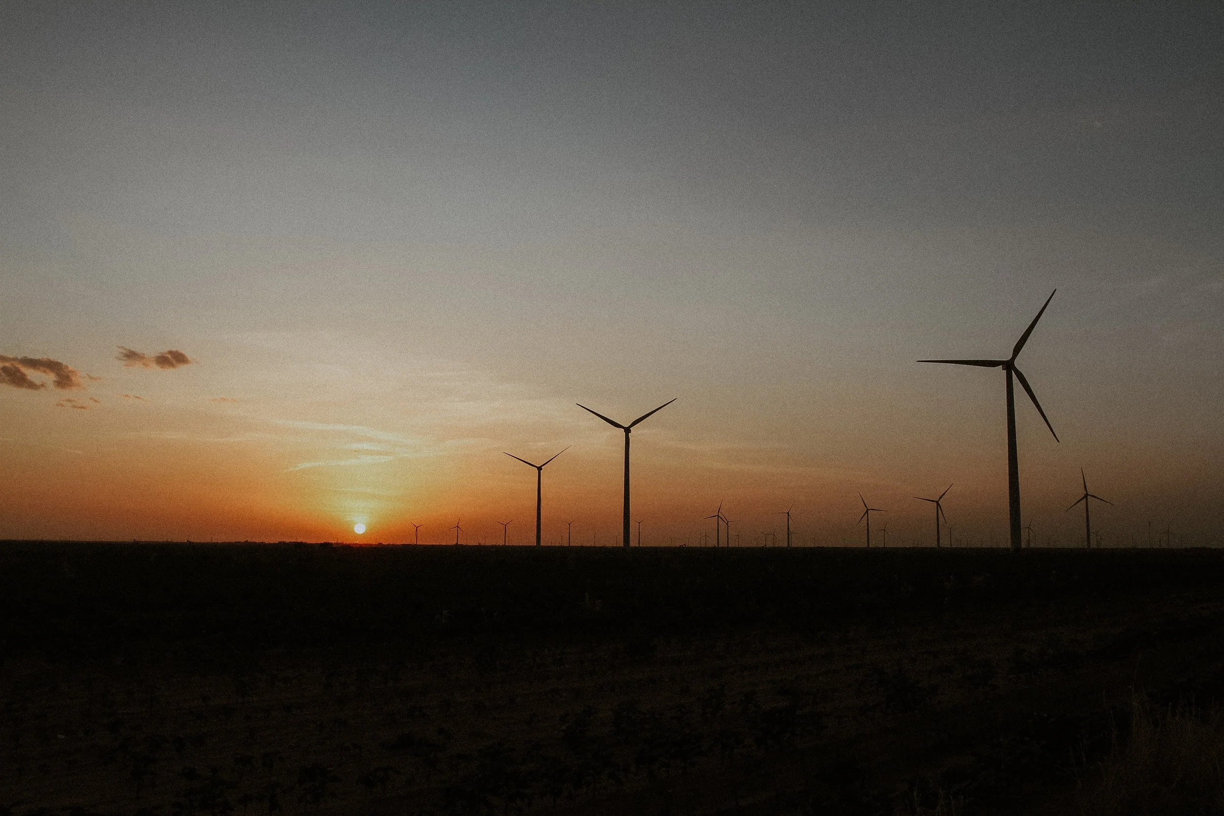 Sunset over a field with wind turbines in the distance.