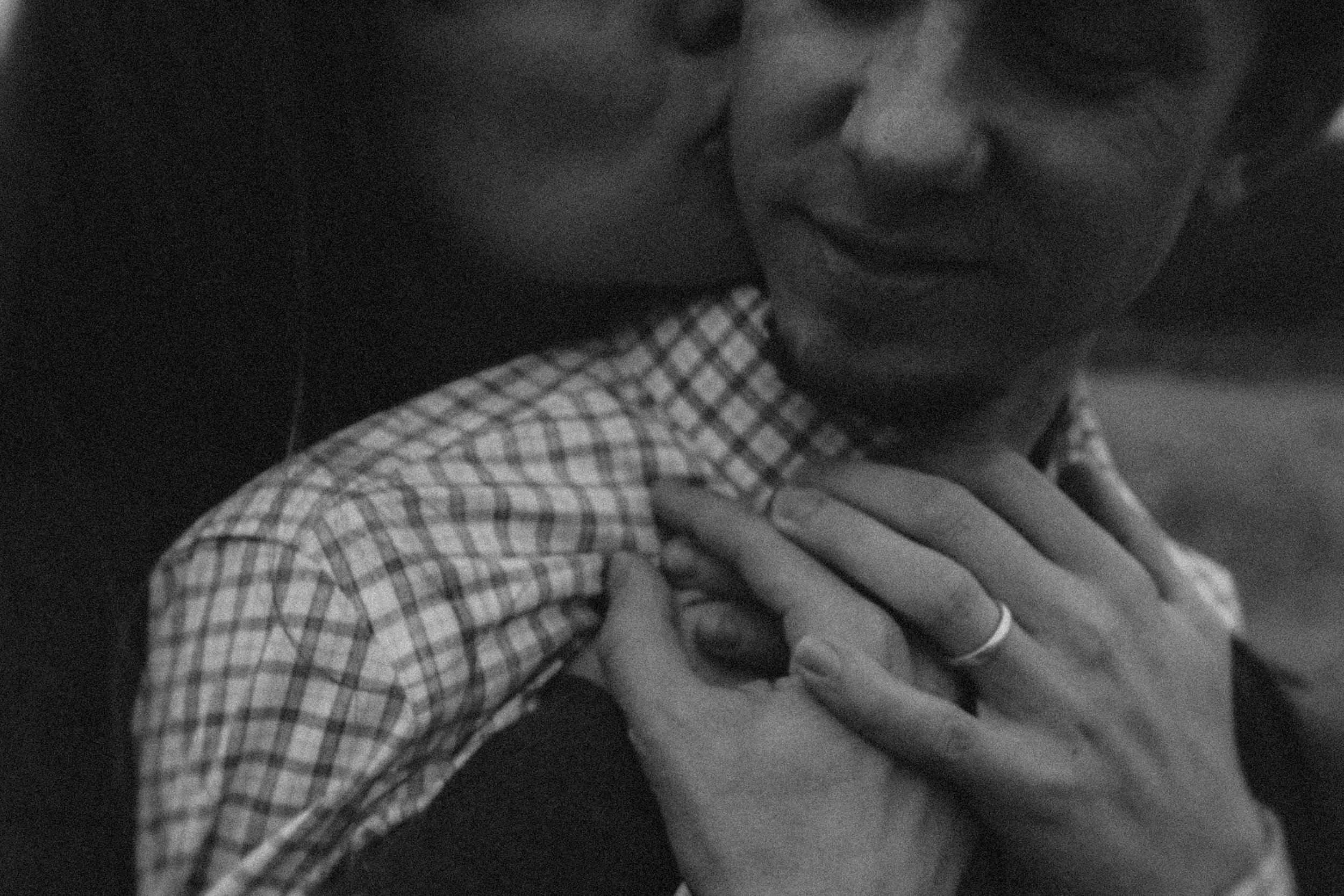 Two people sitting close together, one with a checkered shirt, and pants, with their hand on the other's knee, sharing an intimate moment.
