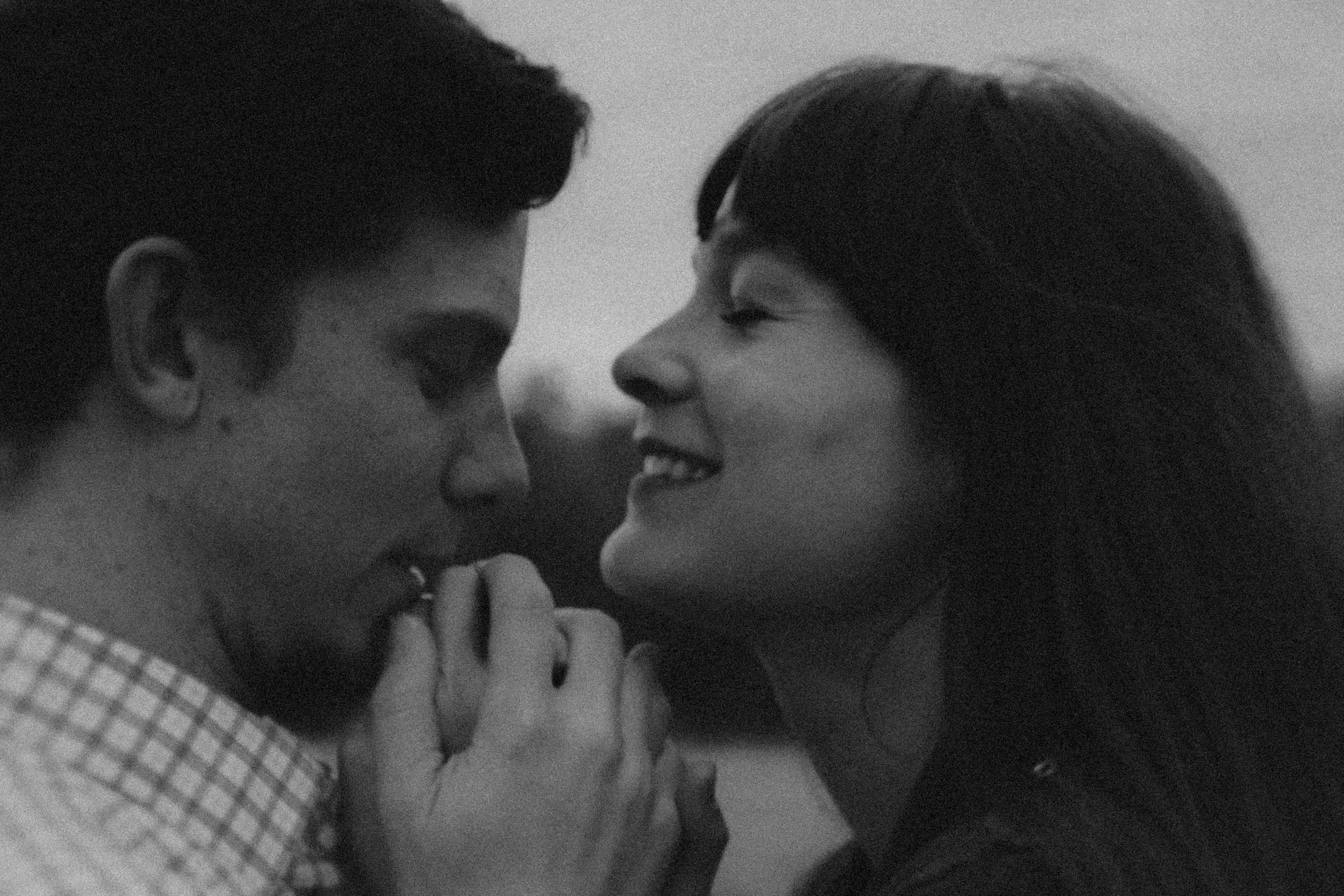 A black and white close-up photo of a couple facing each other, smiling, with their foreheads nearly touching, conveying intimacy and connection.