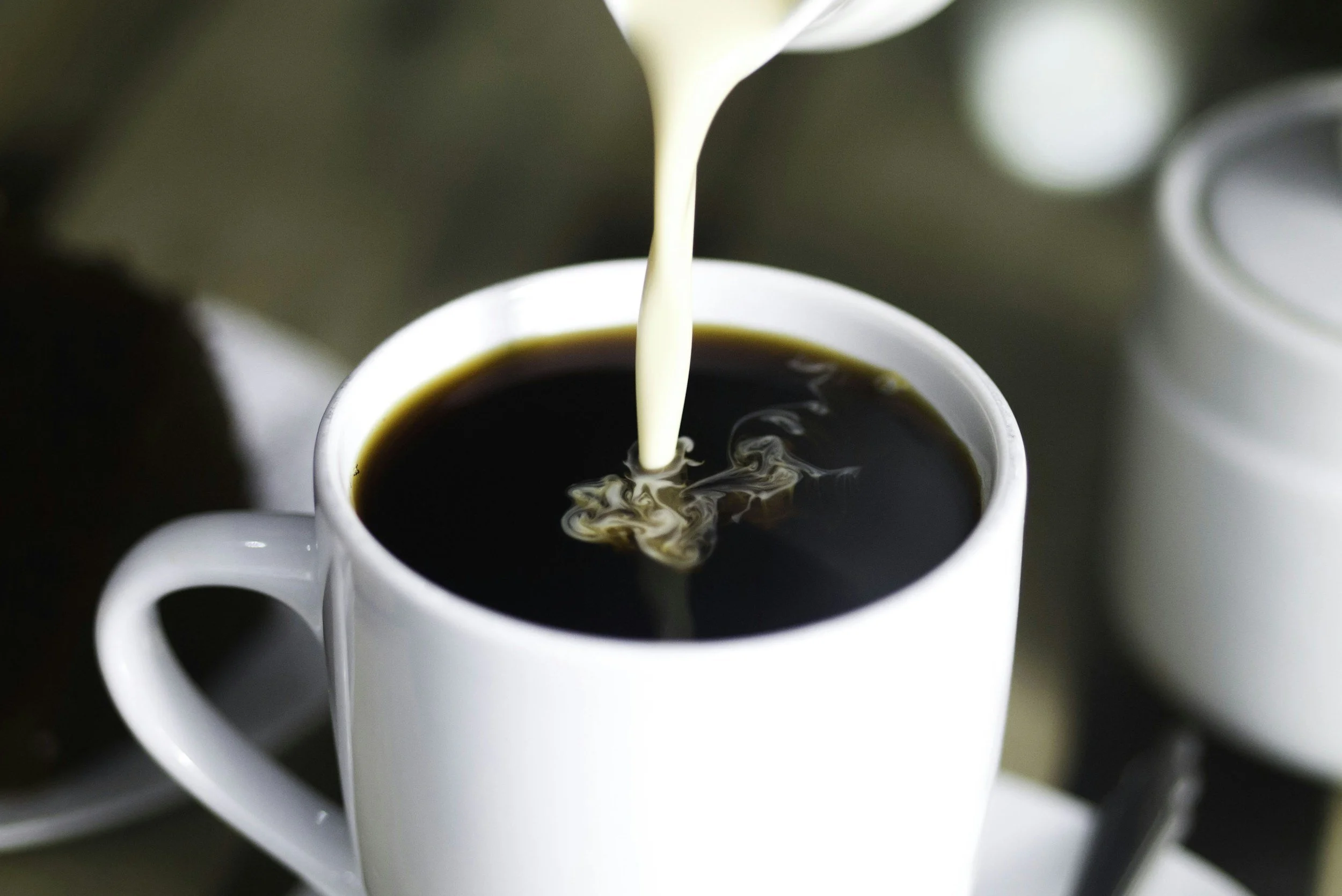 Close-up of hot black coffee being poured into a white ceramic mug.