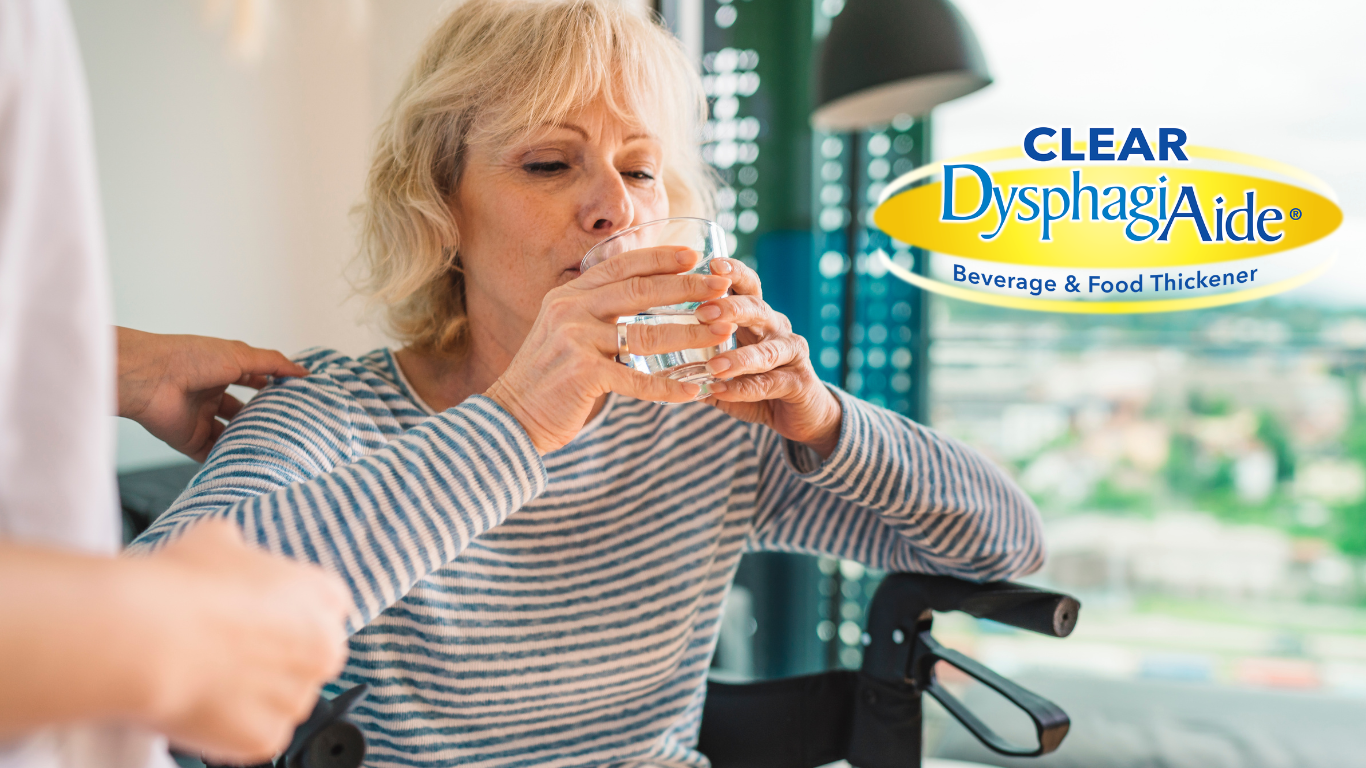 An elderly woman with blonde hair and a striped shirt is sitting in a wheelchair and drinking a glass of water while a caregiver gently places a hand on her shoulder. There is a logo for Clear Dysphagia Aide in the upper right corner.