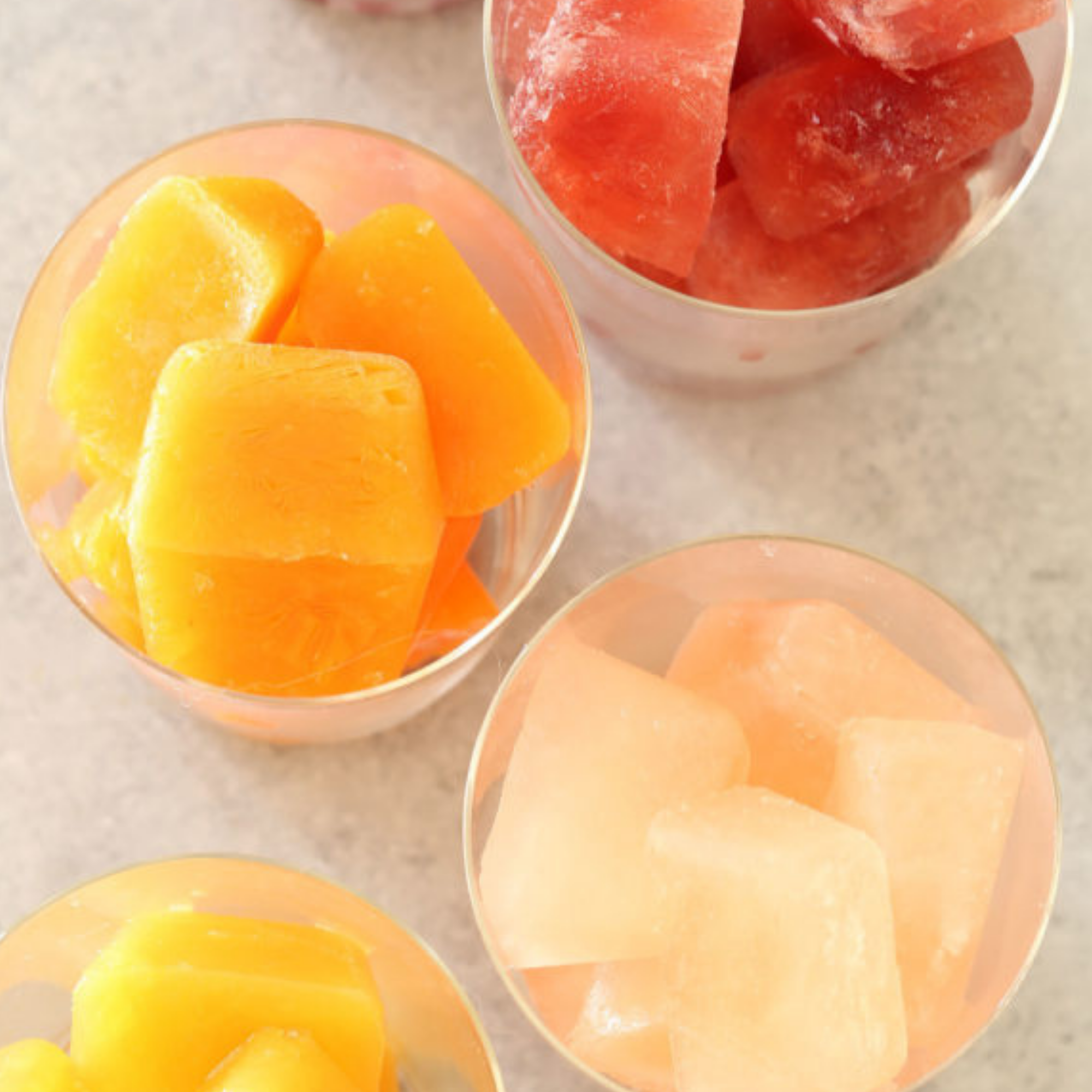 Close-up of two glasses containing different types of fruit cubes; one glass has yellow mango cubes, and the other has red watermelon cubes.