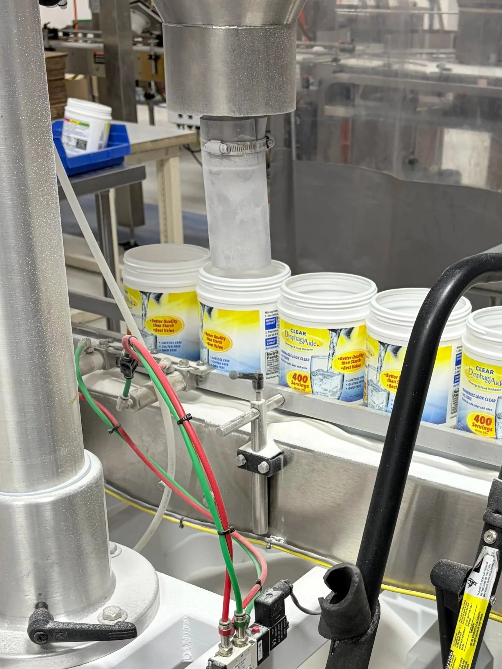 A manufacturing run of Clear DysphagiAide product containers on a conveyer belt.