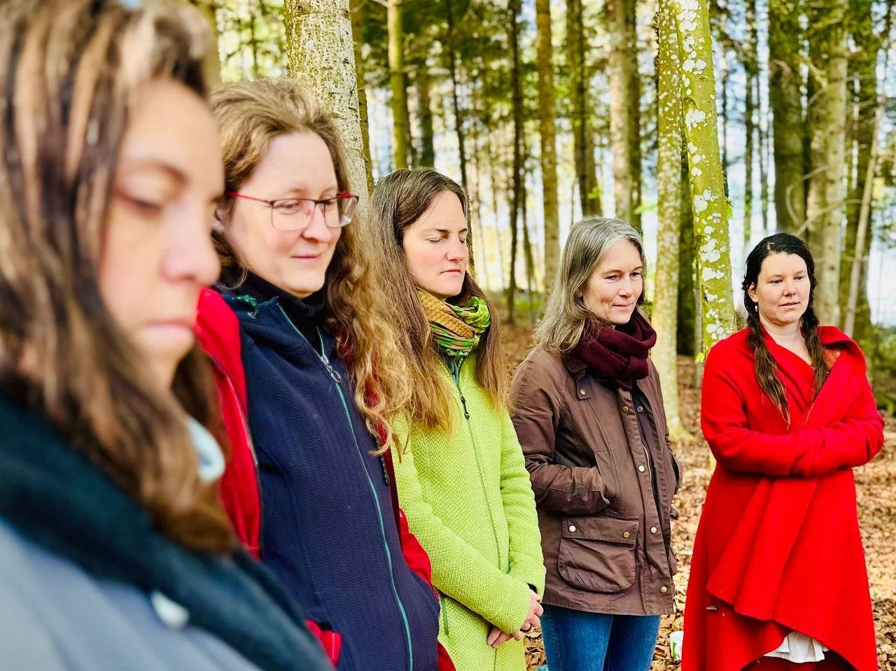 Fünf Frauen stehen mit geschlossenen Augen im Wald und beten oder meditieren.