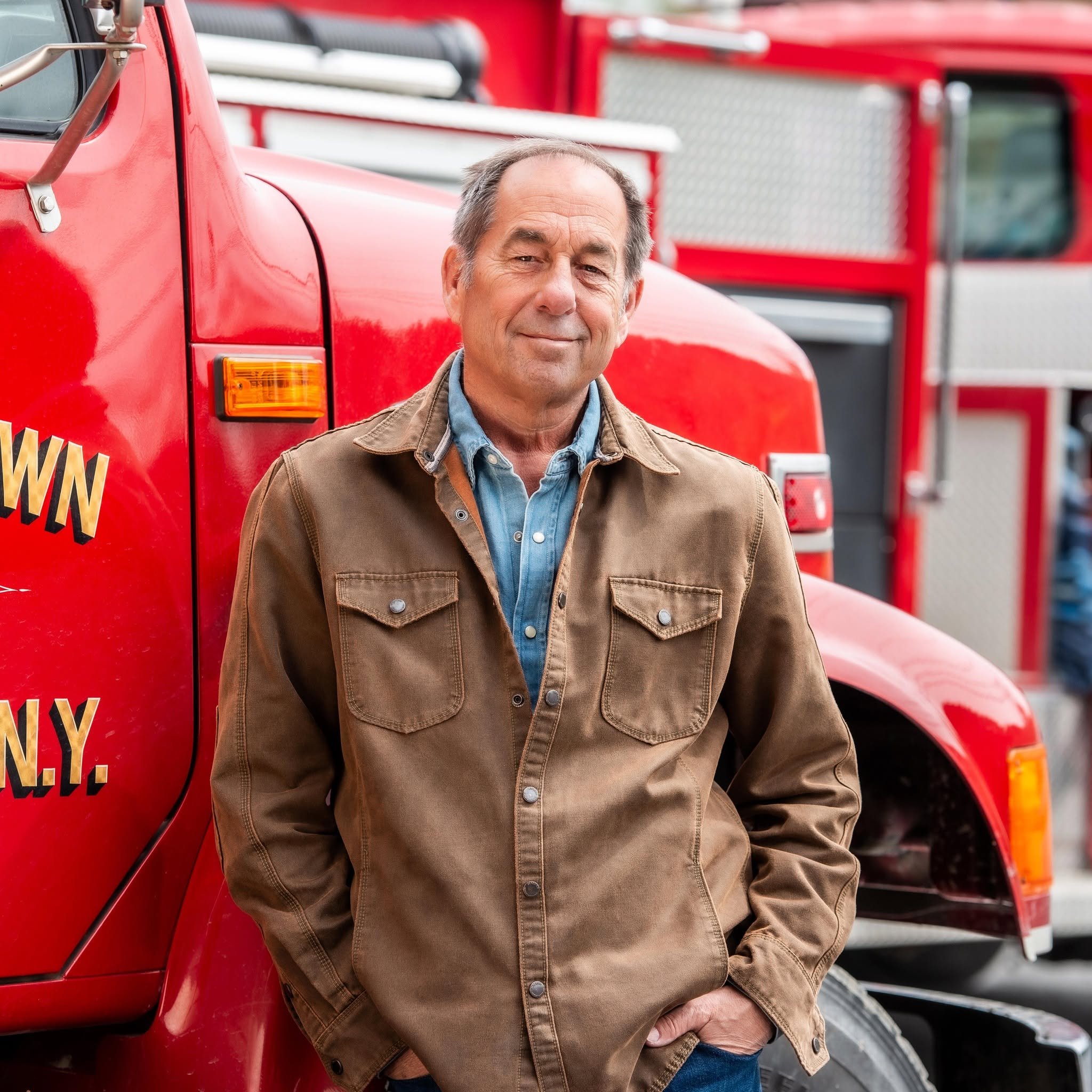 Winemaker Joseph Carr is in a denim shirt and brown jacket, leaning against a red fire truck.
