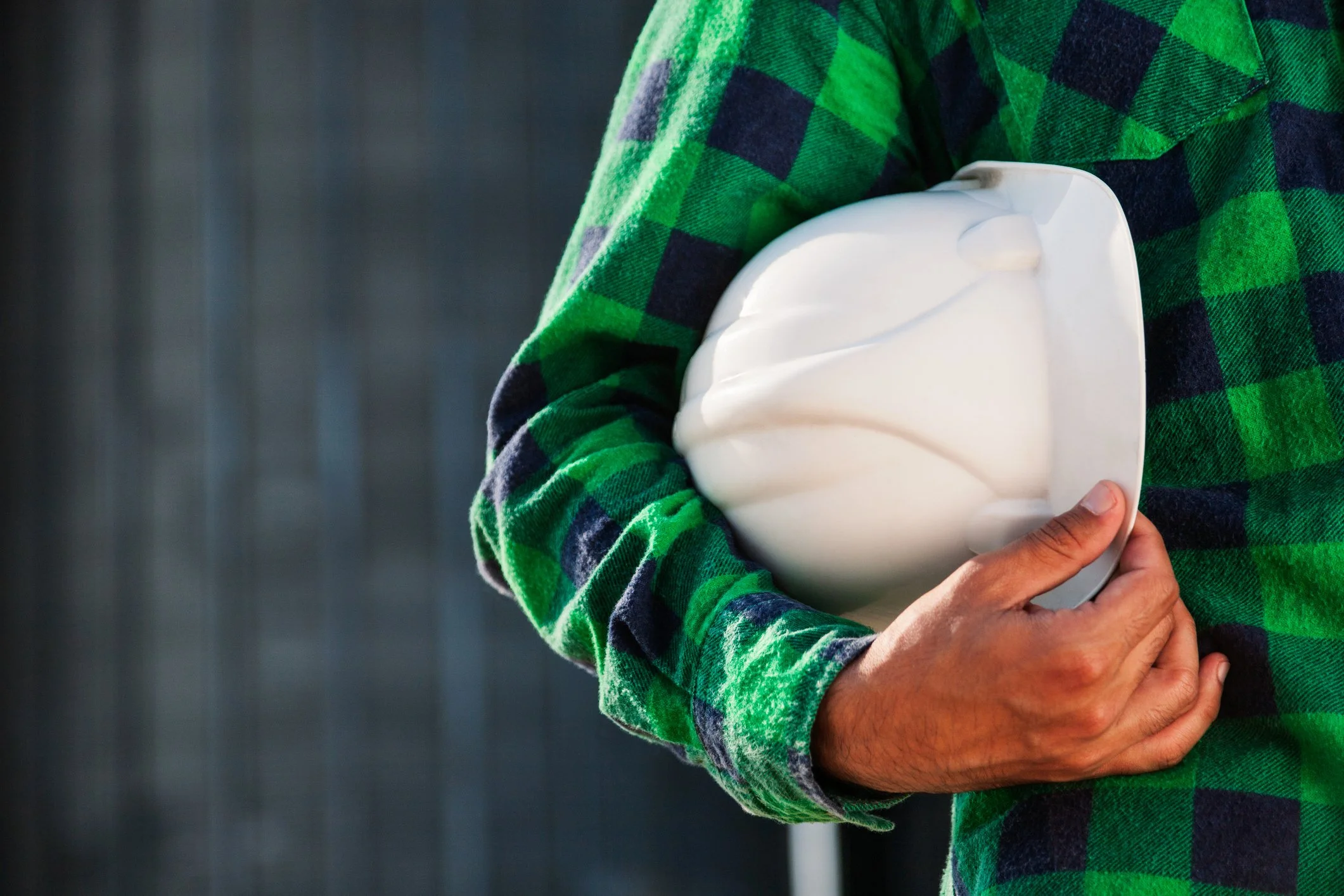 Person wearing a green and black plaid shirt holding a white helmet.