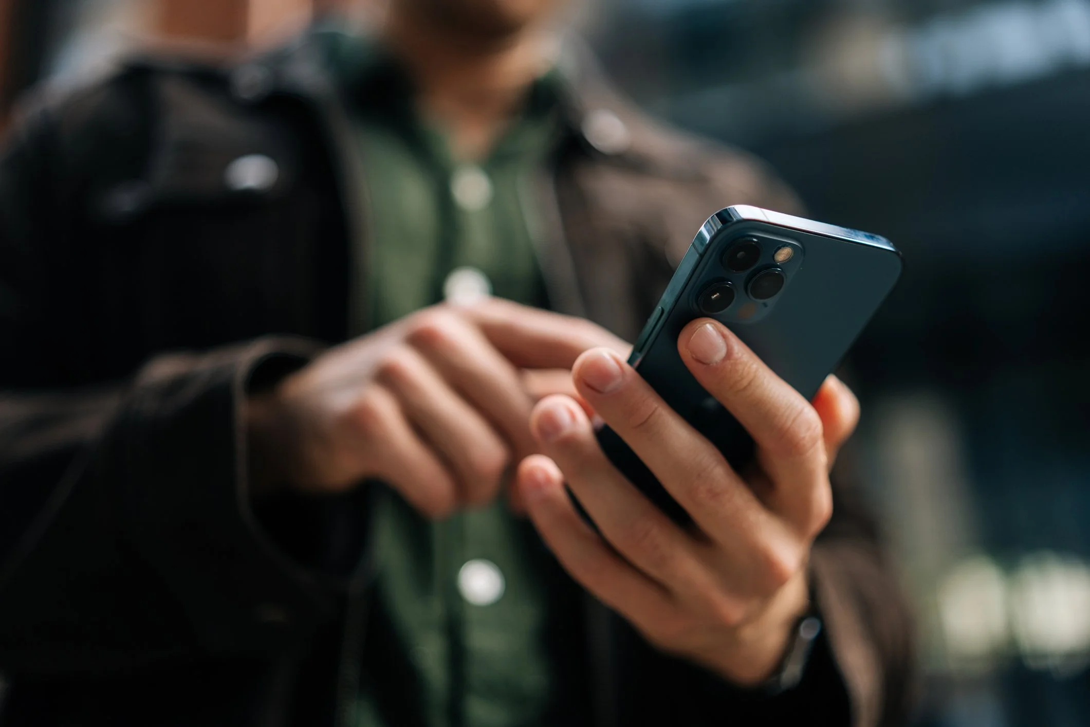 Close-up of person holding a smartphone, wearing a black jacket and green shirt.