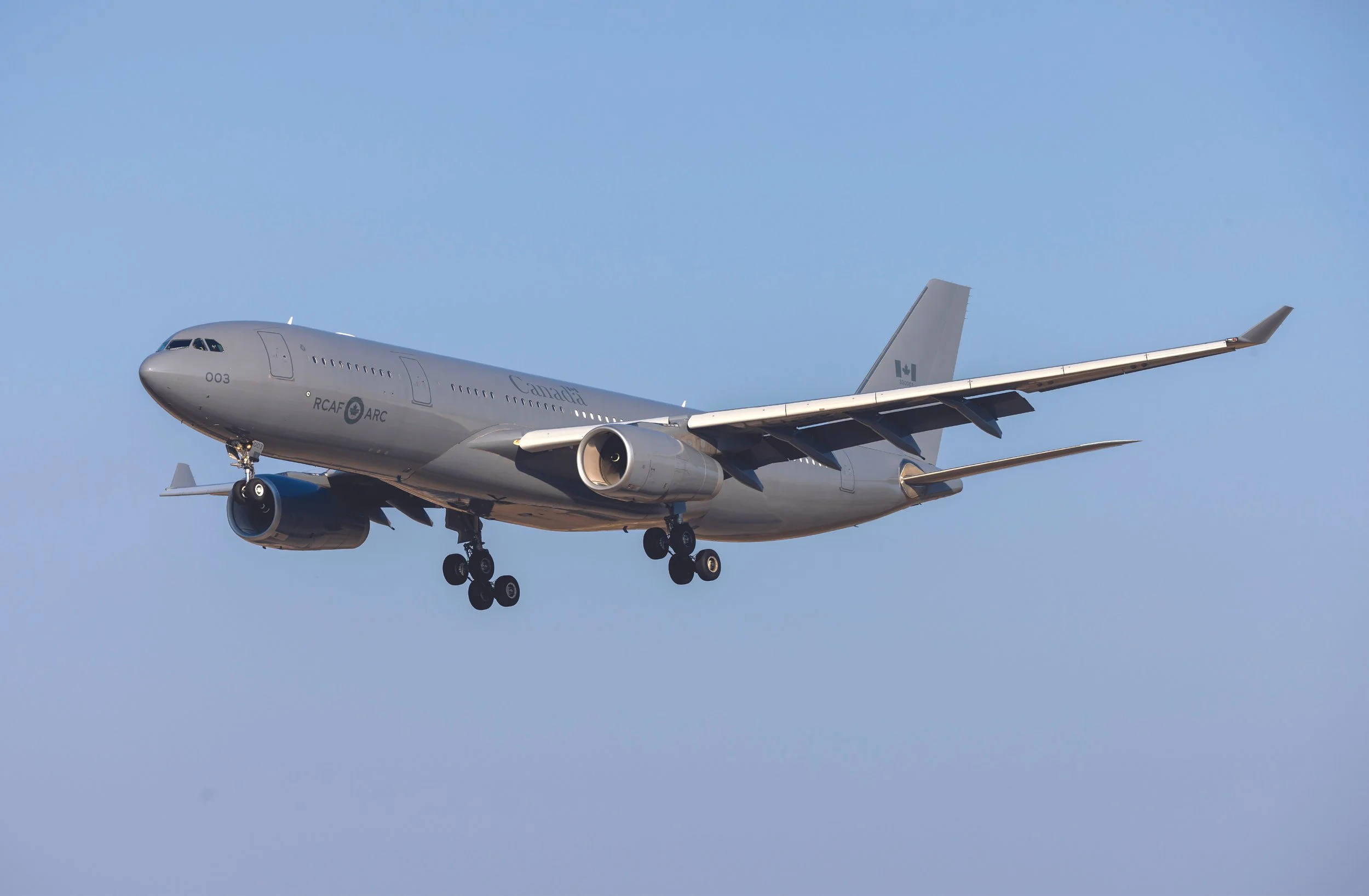 A Canadian military aircraft in flight with the landing gear extended, flying against a blue sky.