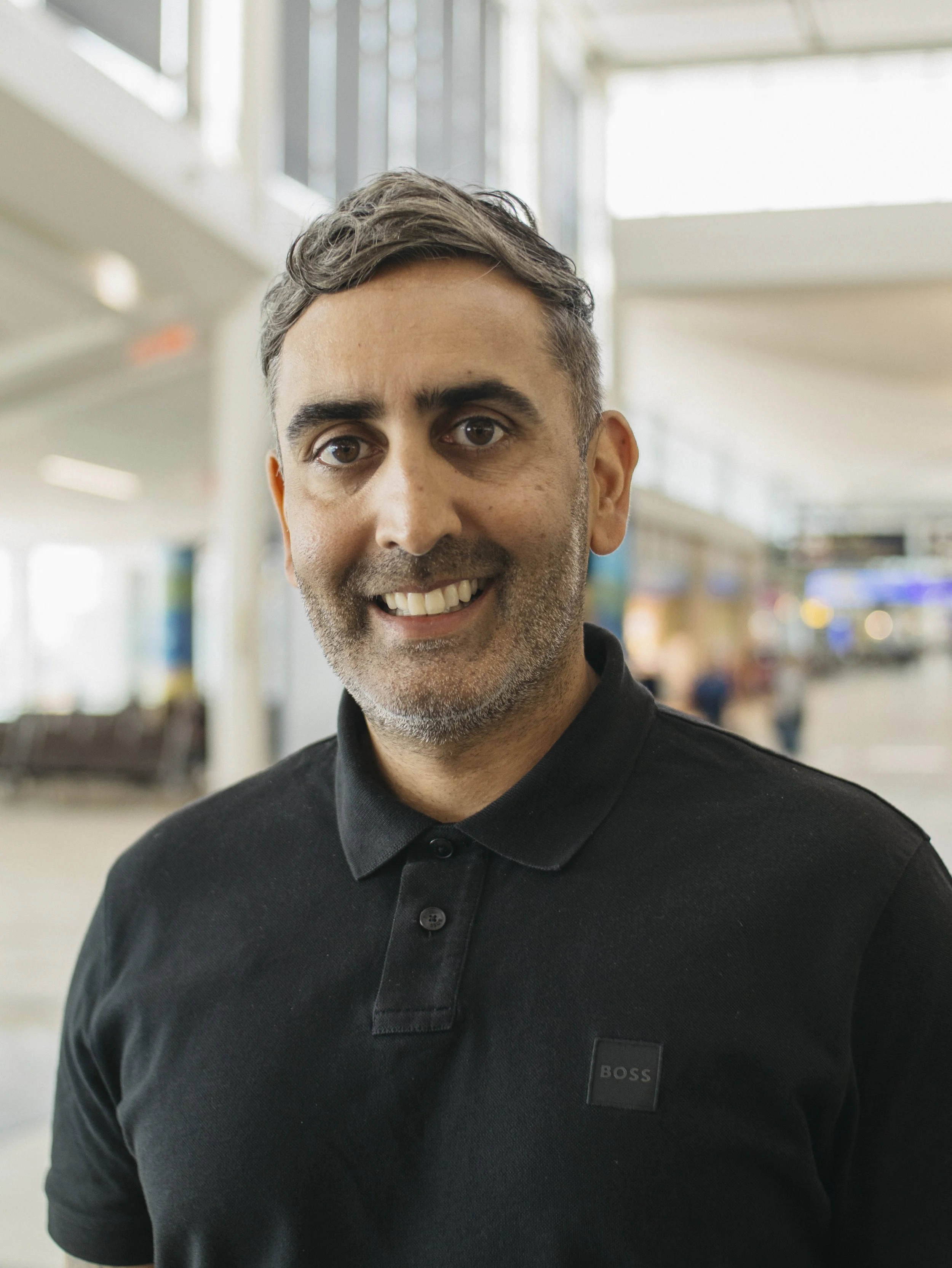 Close-up of a smiling middle aged man in a black top, in an indoor setting with blurred background.
