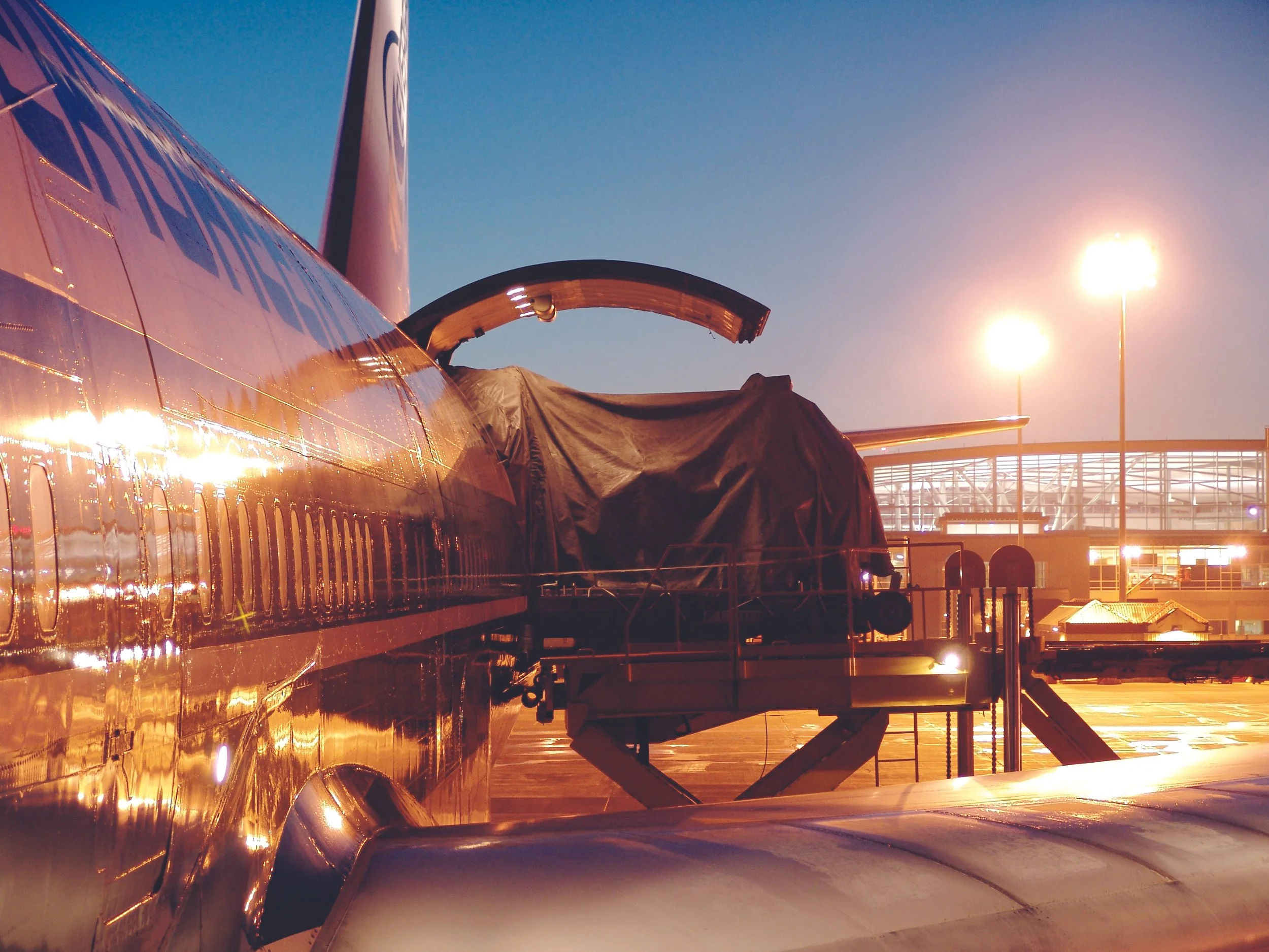 Airplane parked at gate during sunset with tarmac and airport structures in the background.