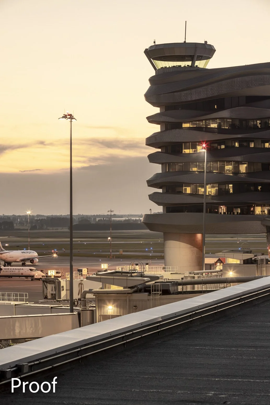 Airport control tower at sunset with planes on the tarmac and runway lights in the background.