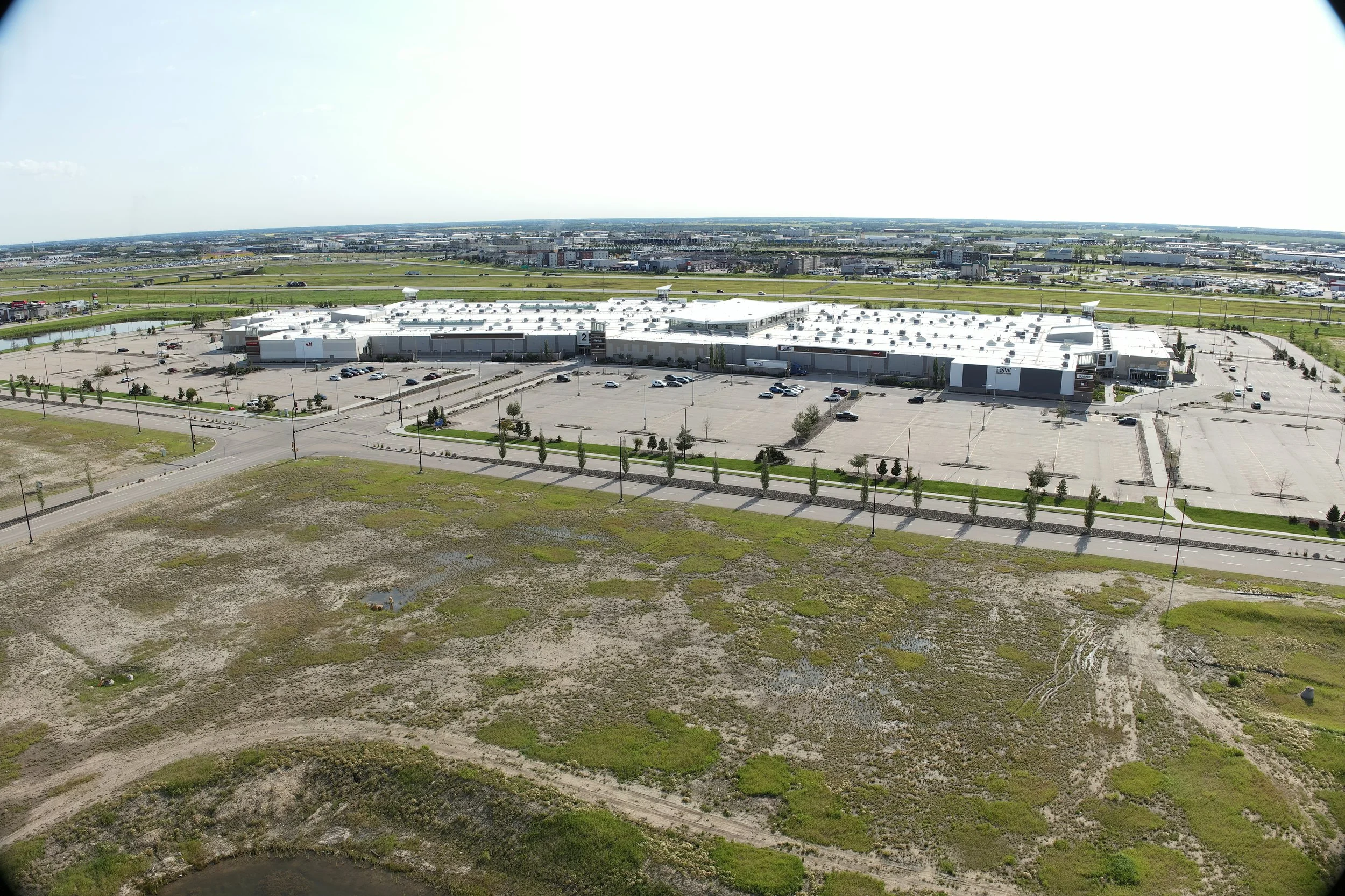 Aerial view of a large shopping mall with parking lot, surrounded by roads and green areas.