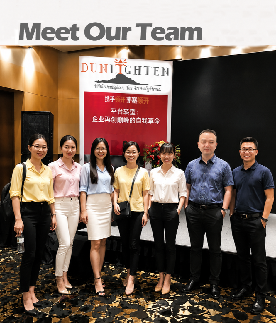 Eight diverse people standing on stage in front of a banner that reads 'Meet Our Team' and 'DUN LIGHTEN.' The group includes five women and three men dressed in business casual attire, smiling for the photo at a professional event.