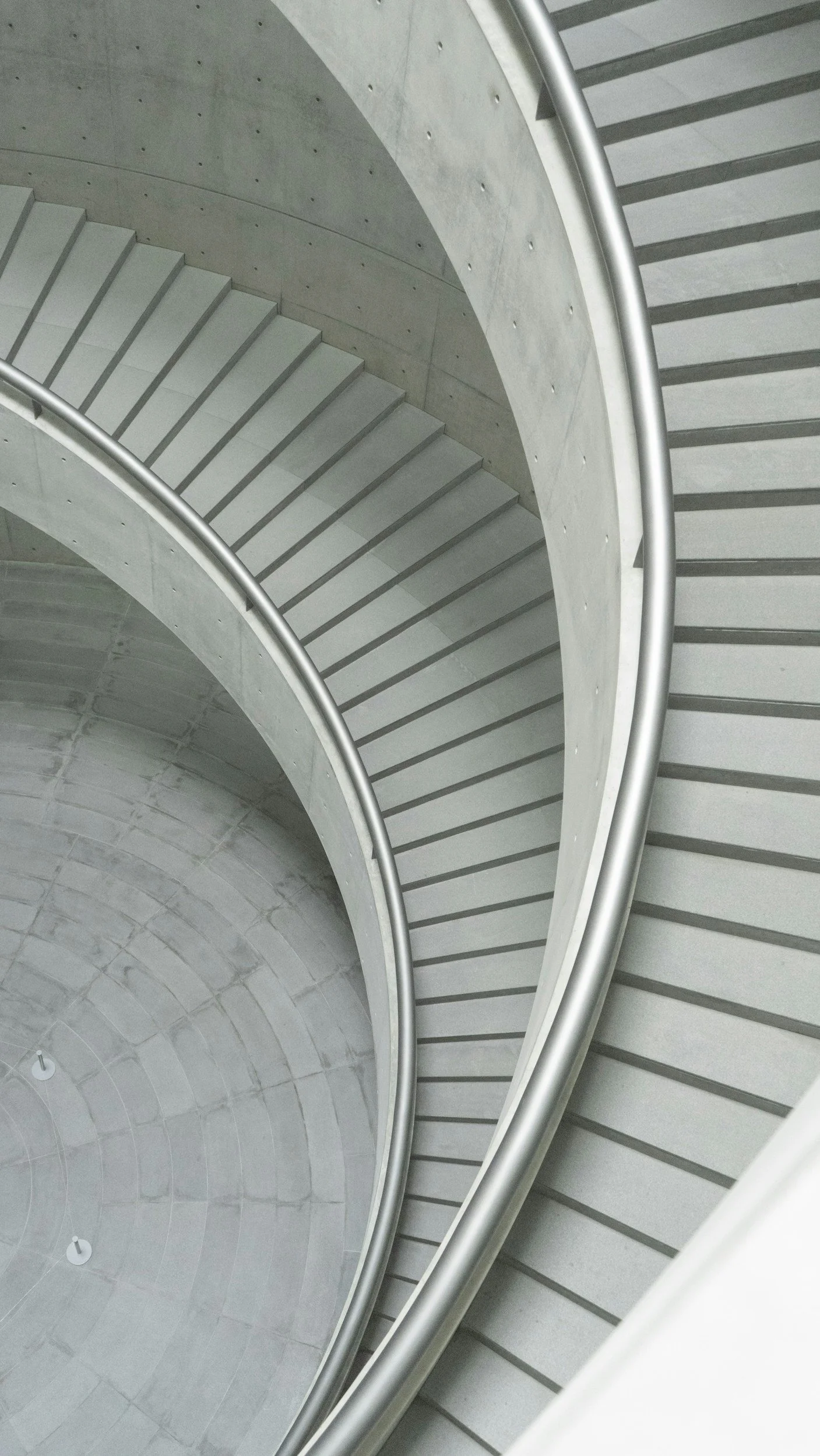 View of a modern, spiraling concrete stairwell with metal handrails.