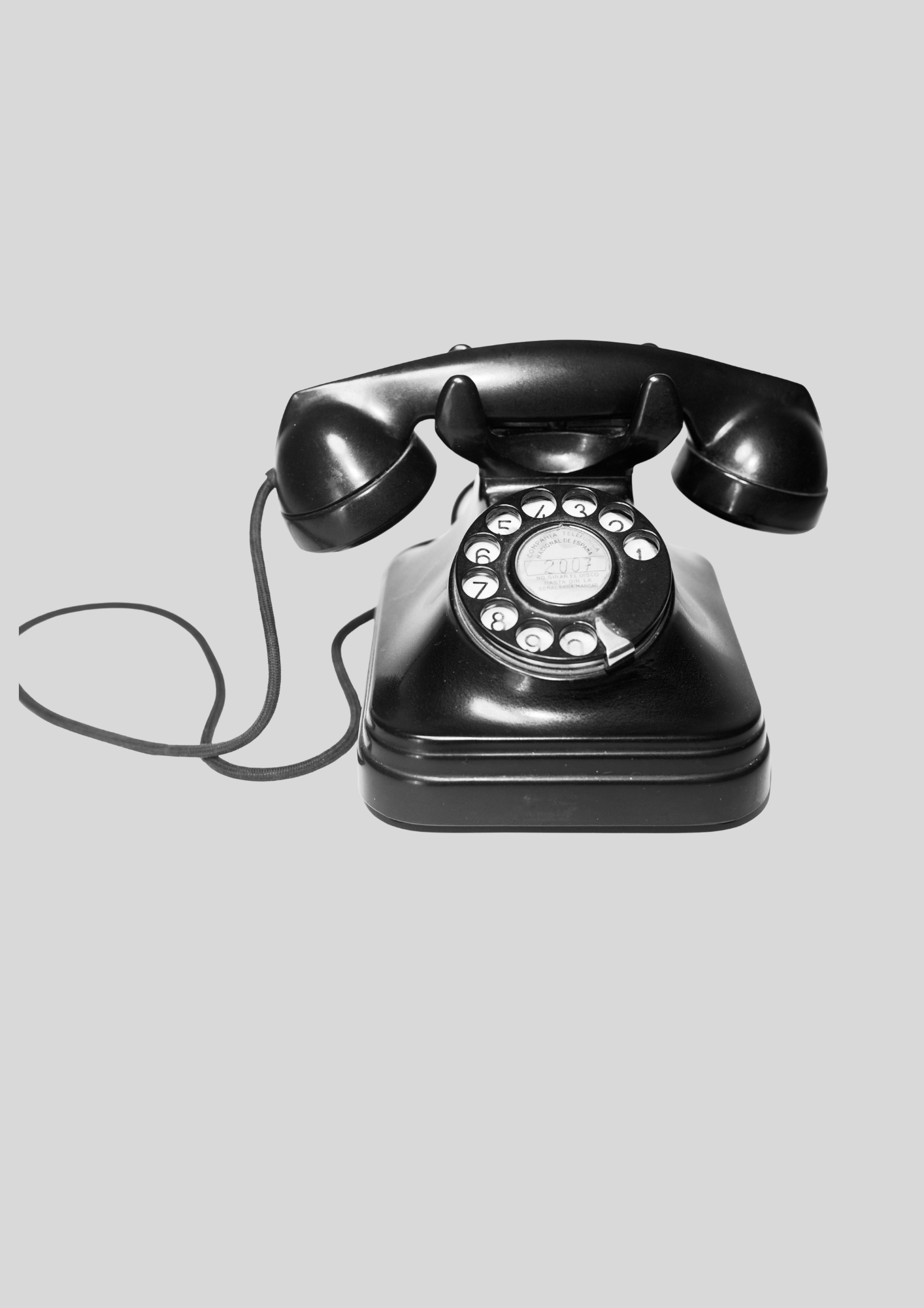 A black rotary dial telephone with a cord on a light gray background.