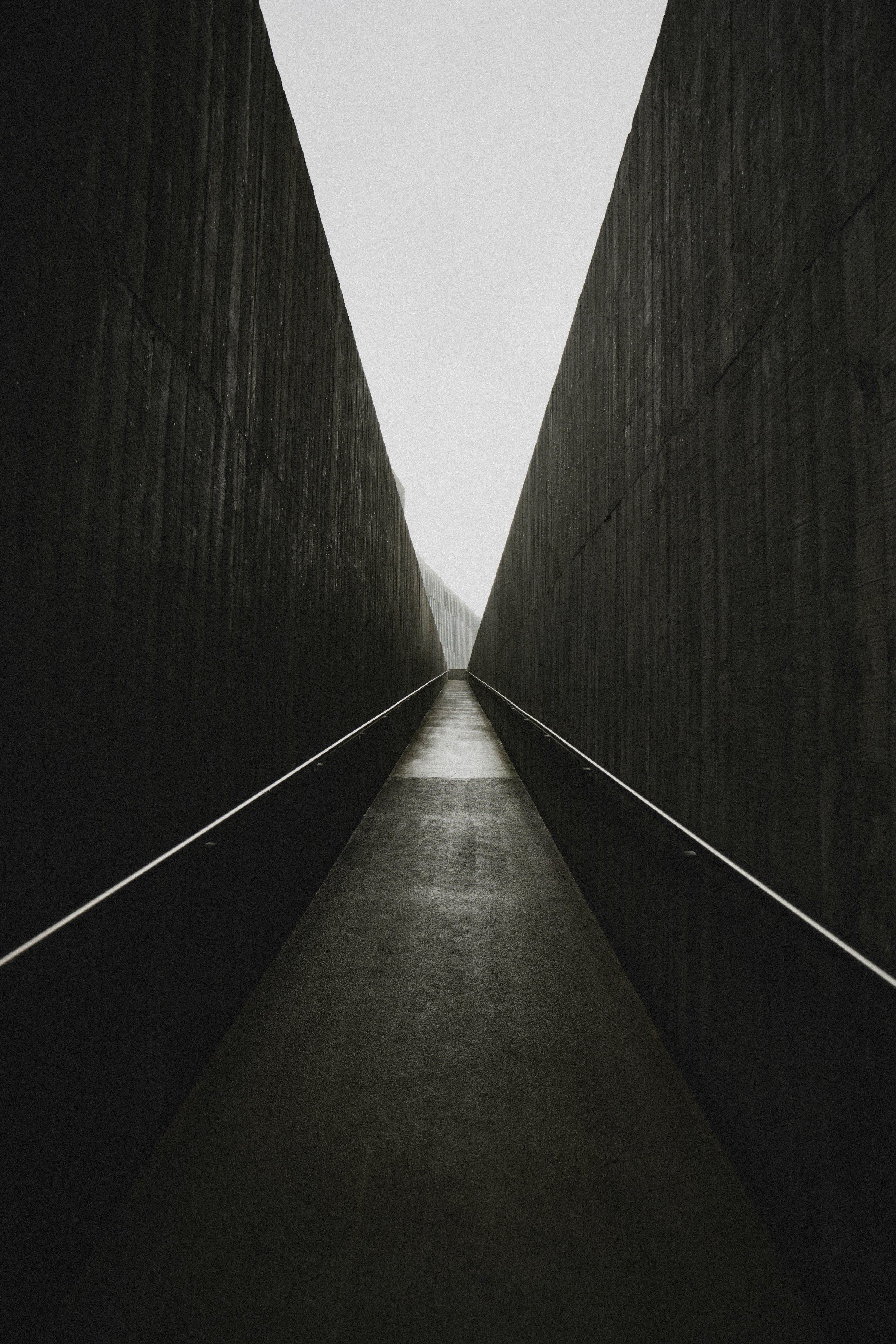 A narrow, symmetrical pathway between two tall, dark stone walls with a light sky above, leading the eye to a distant, foggy horizon.