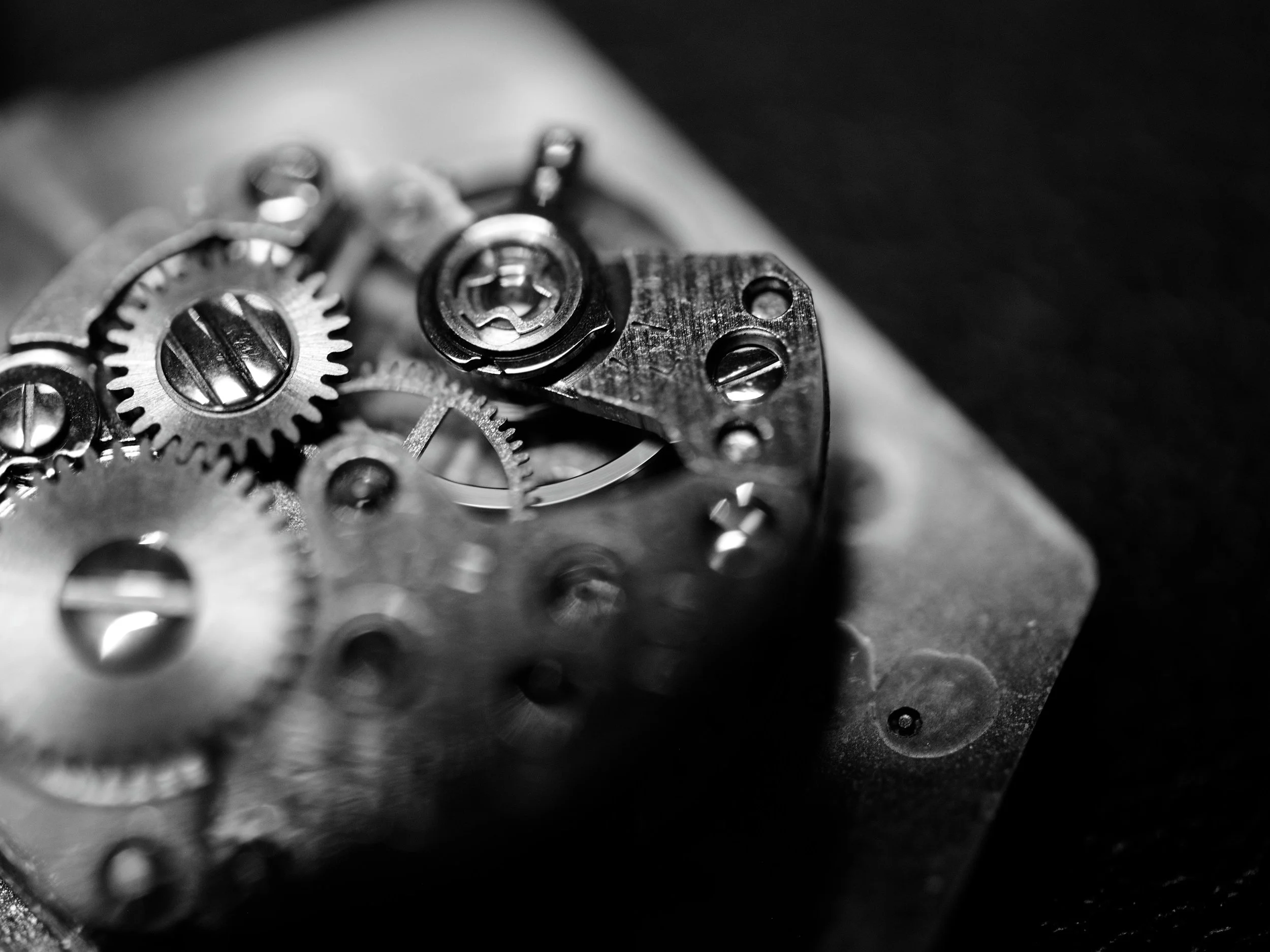 Close-up of the internal gears and mechanical parts of a watch or clock in black and white.