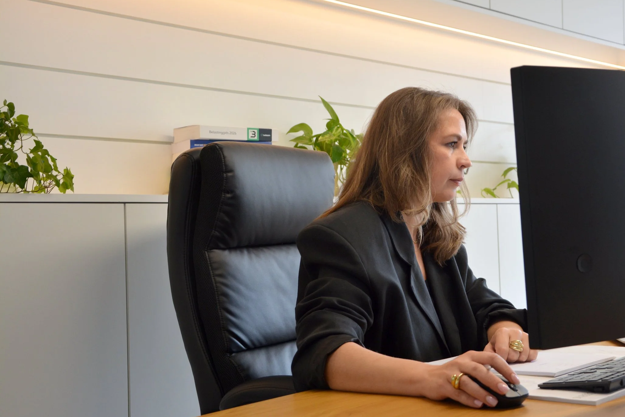 Vrouw die op een computer werkt op een kantoor, omgeven door planten.