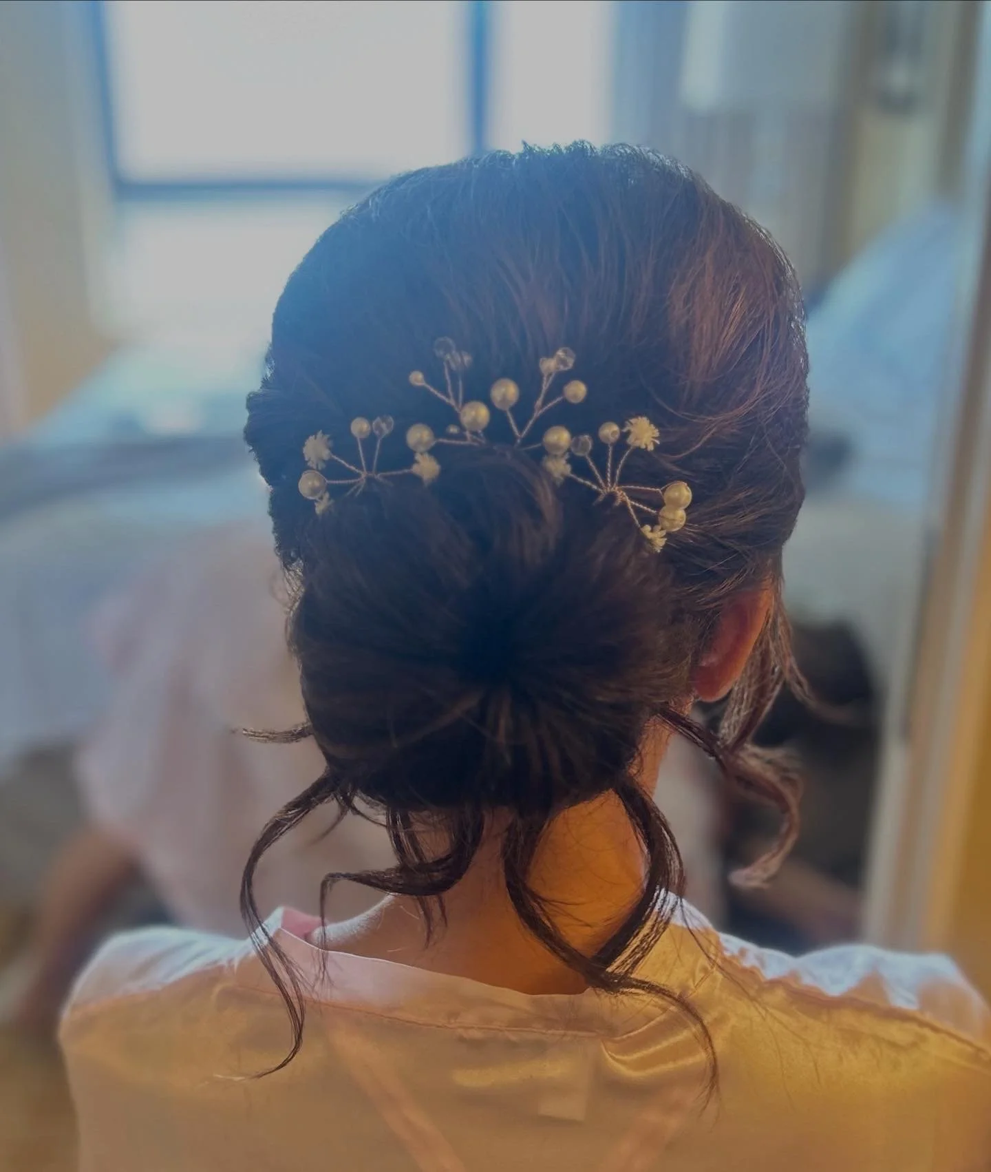 Woman with dark hair styled in an elegant updo adorned with small white flowers and pearl-like decorations.