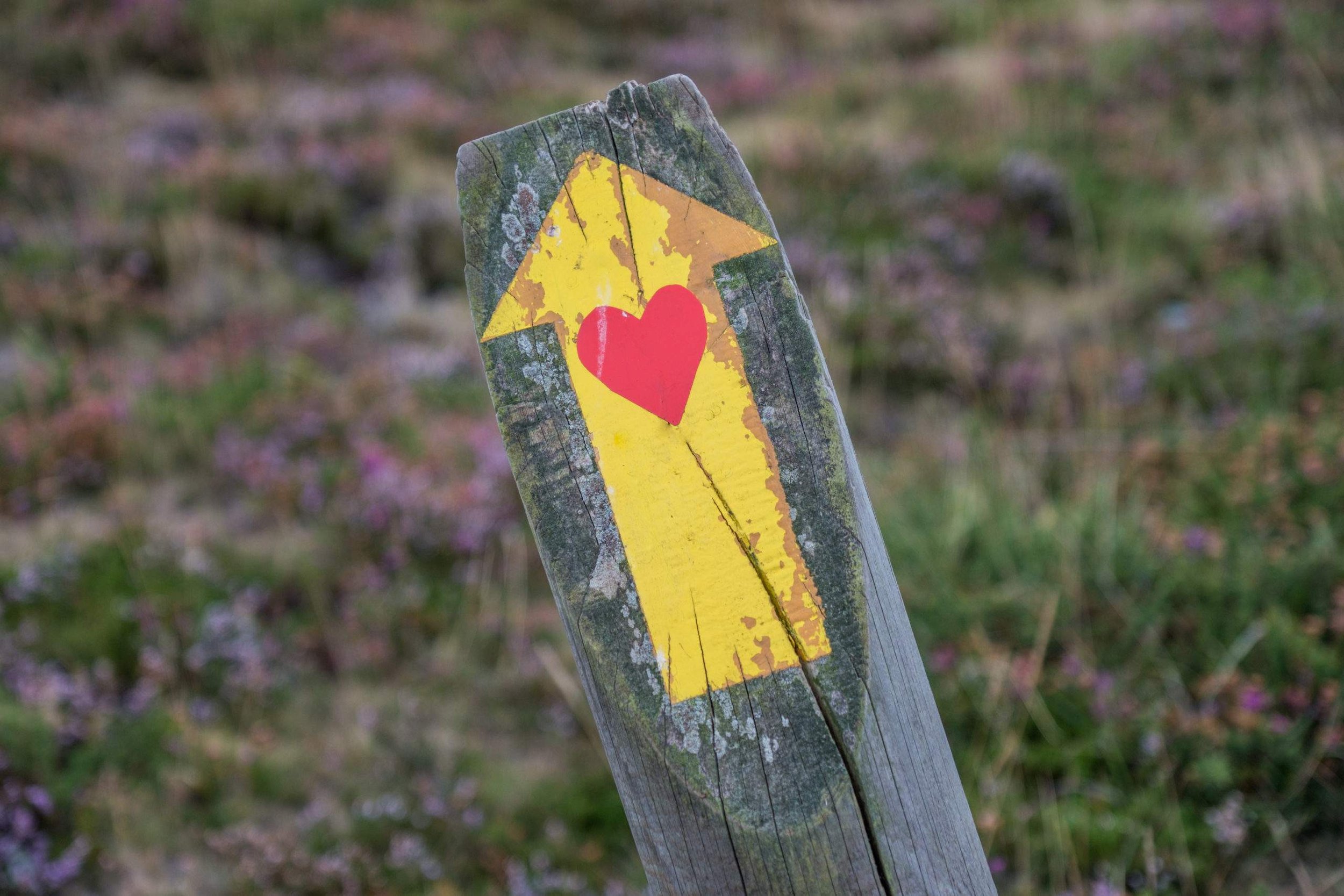 A weathered wooden post painted with a yellow background, featuring a red heart and a yellow star.