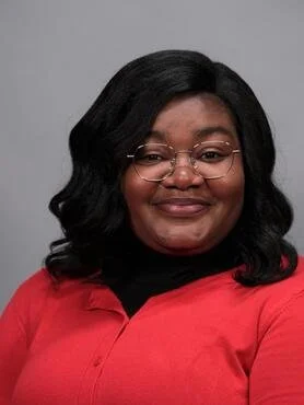 A woman with shoulder-length black hair and glasses, smiling, wearing a red shirt with a black collar against a gray background.