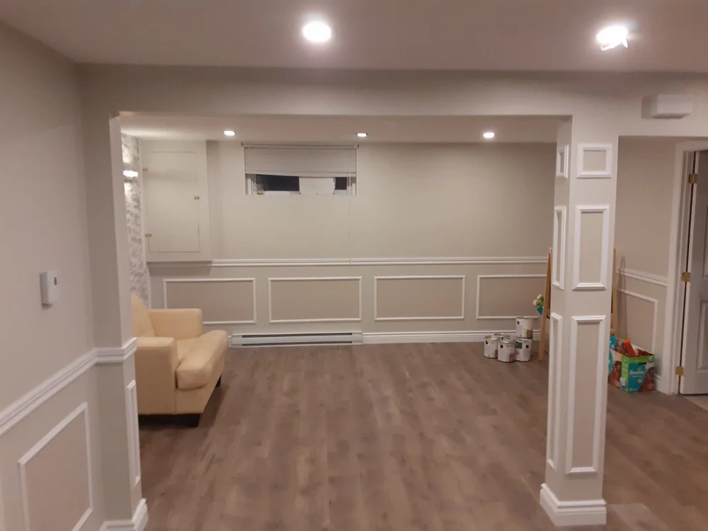 Finished basement with white decorative wainscoting and wood floor