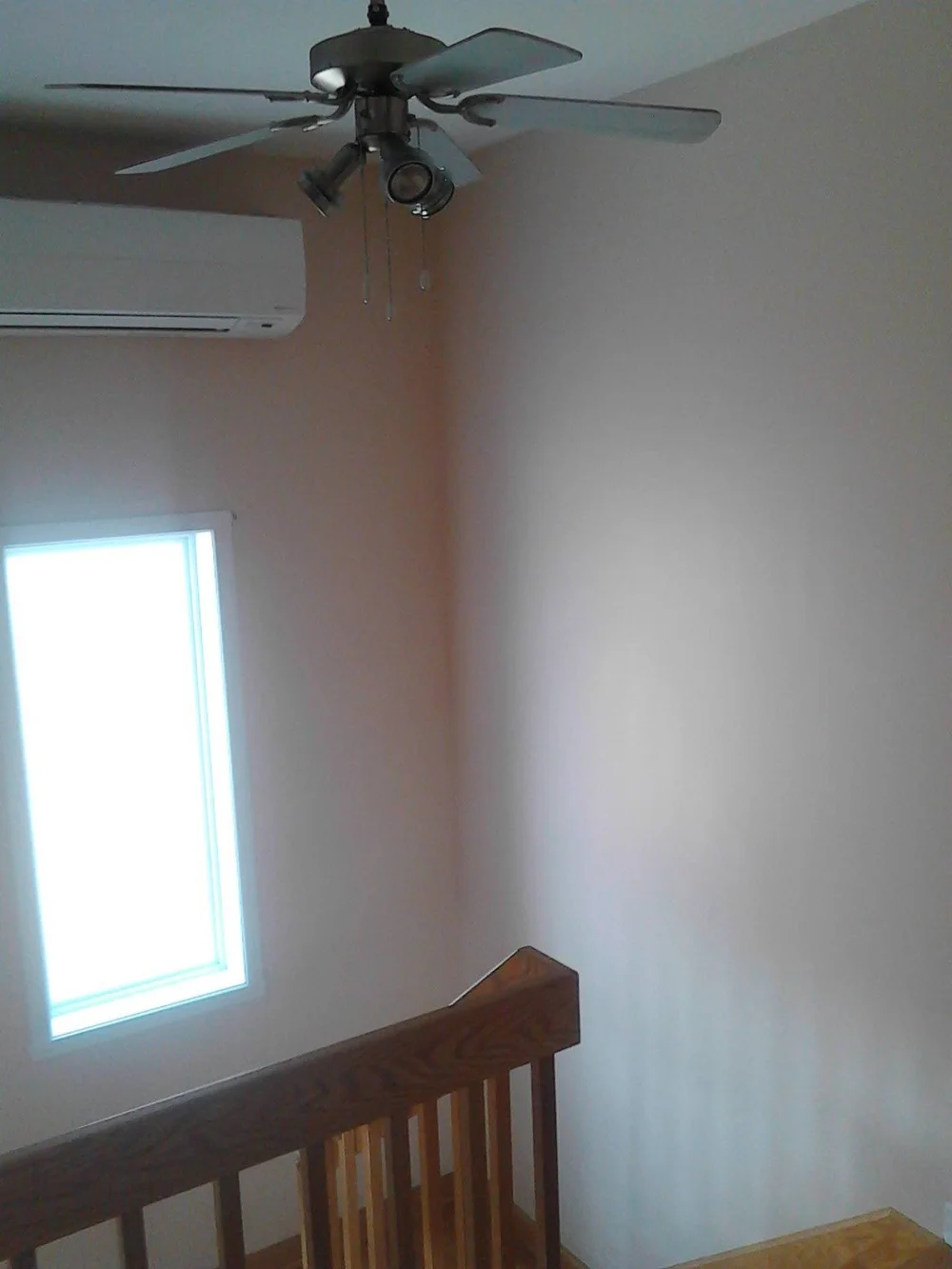 High stairwell wall beside a wooden railing and ceiling fan