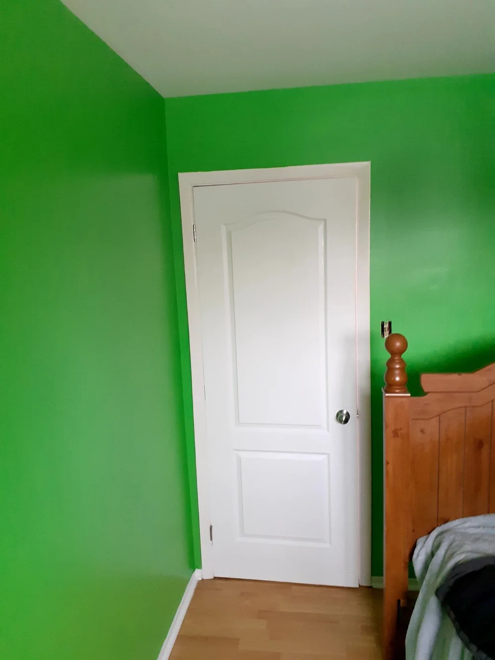 Bedroom with bright green walls, white door and wooden bed