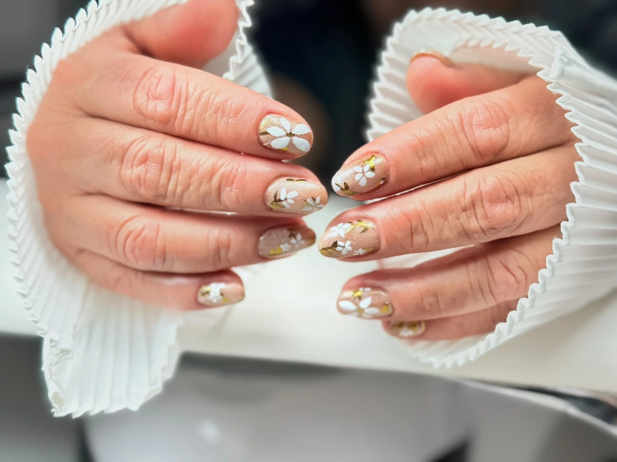 Nahaufnahme von Händen mit floralen Nageldesigns, die in einem weißen, röhrenförmigen Kunststoffbehälter gehalten werden.