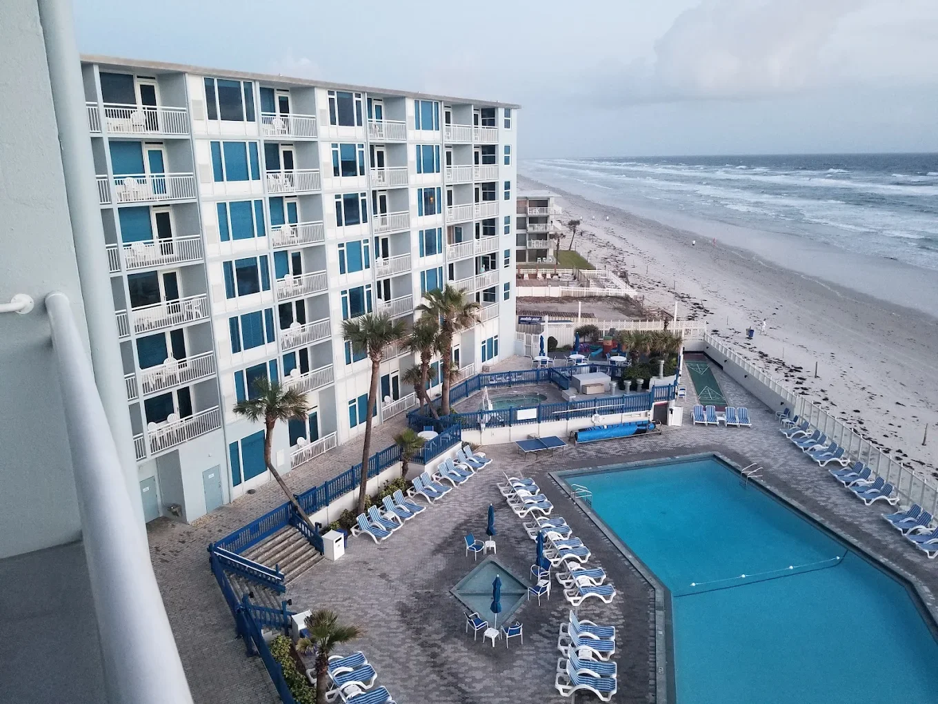 View of Islander Beach Resort beachfront with multiple balconies, a swimming pool surrounded by lounge chairs, and an ocean beach in the background.