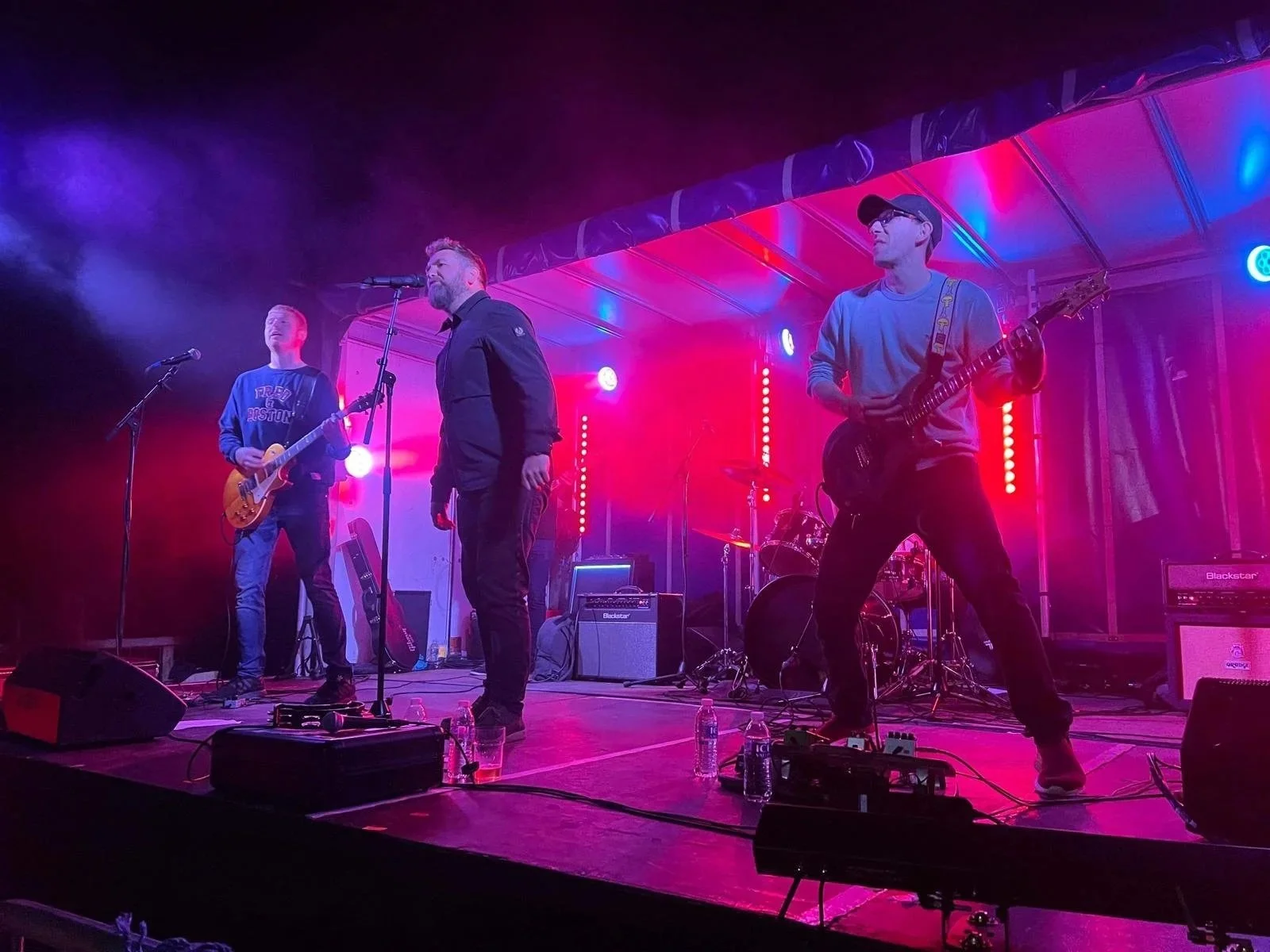 A live rock pop and idie band performs on stage with colourful lighting and musical equipment, including guitars and drums.