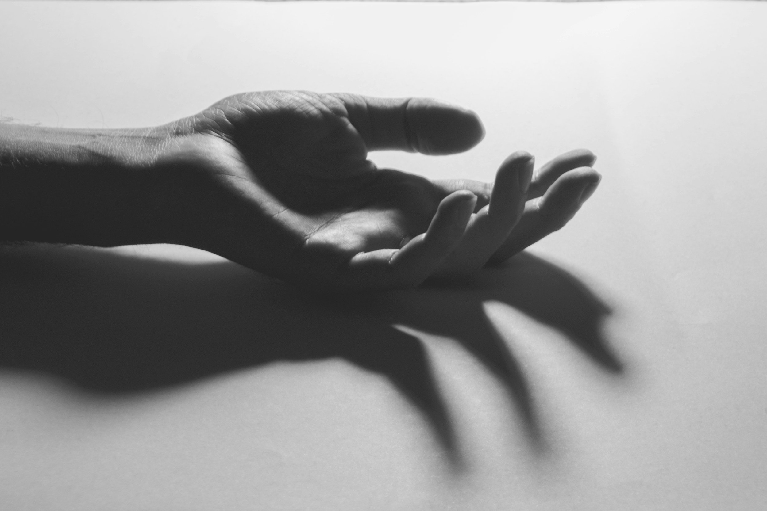 Black and white photo of a hand with fingers extended, casting a shadow on a flat surface.