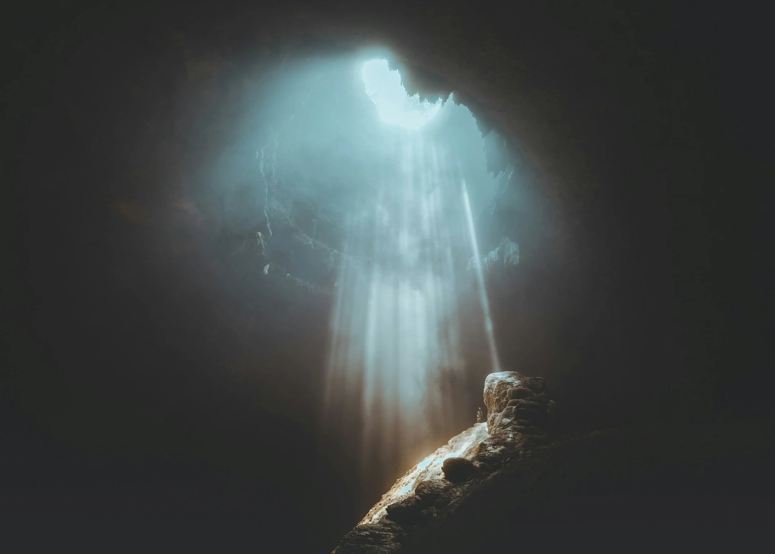 Sunlight streaming through a large opening in a cave, illuminating the interior with beams of light and casting shadows on the rocky walls and floor.