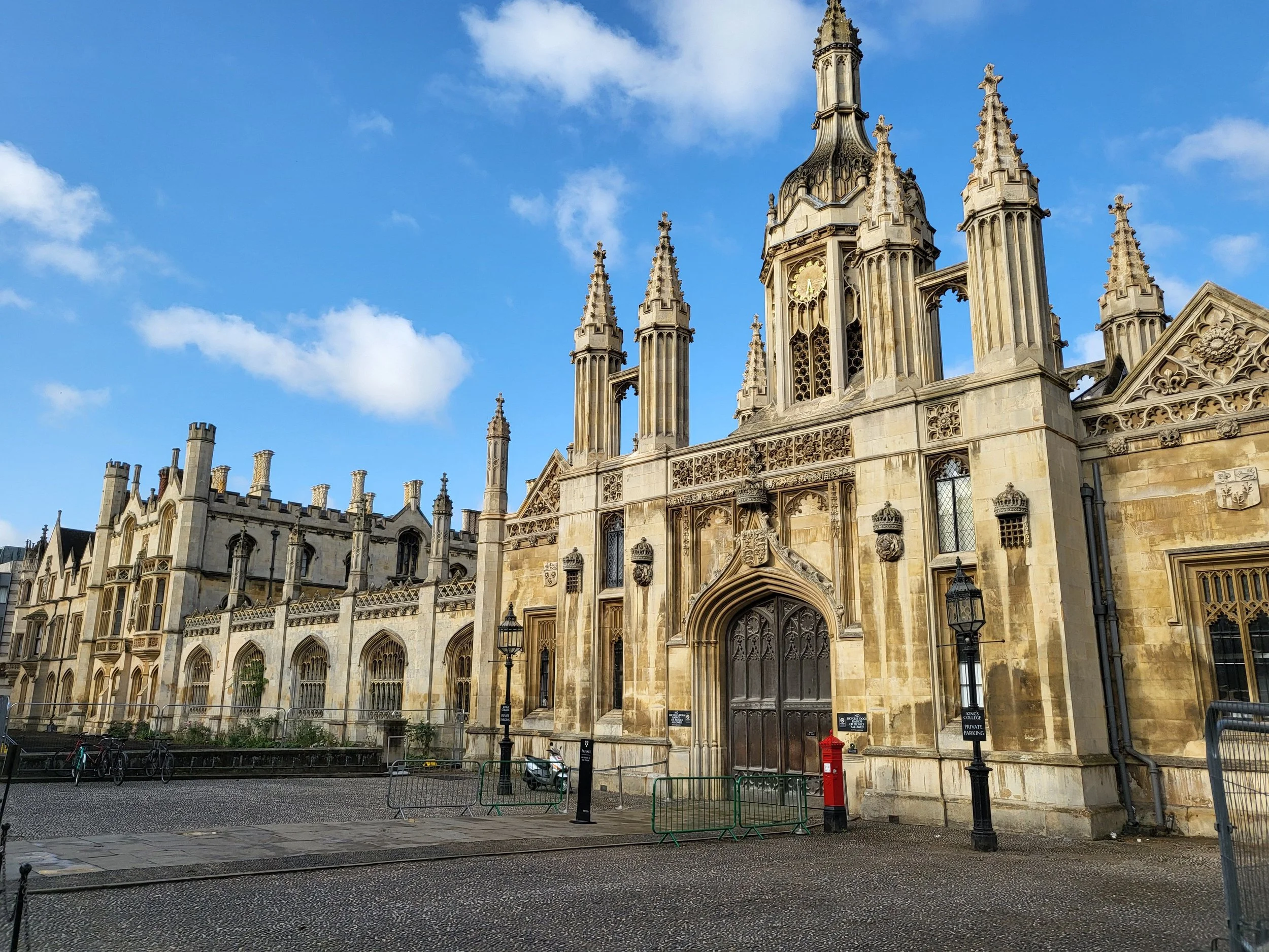 A historic stone building with Gothic architectural features, tall spires, ornate windows, and a clock on the facade, set against a blue sky with some clouds.