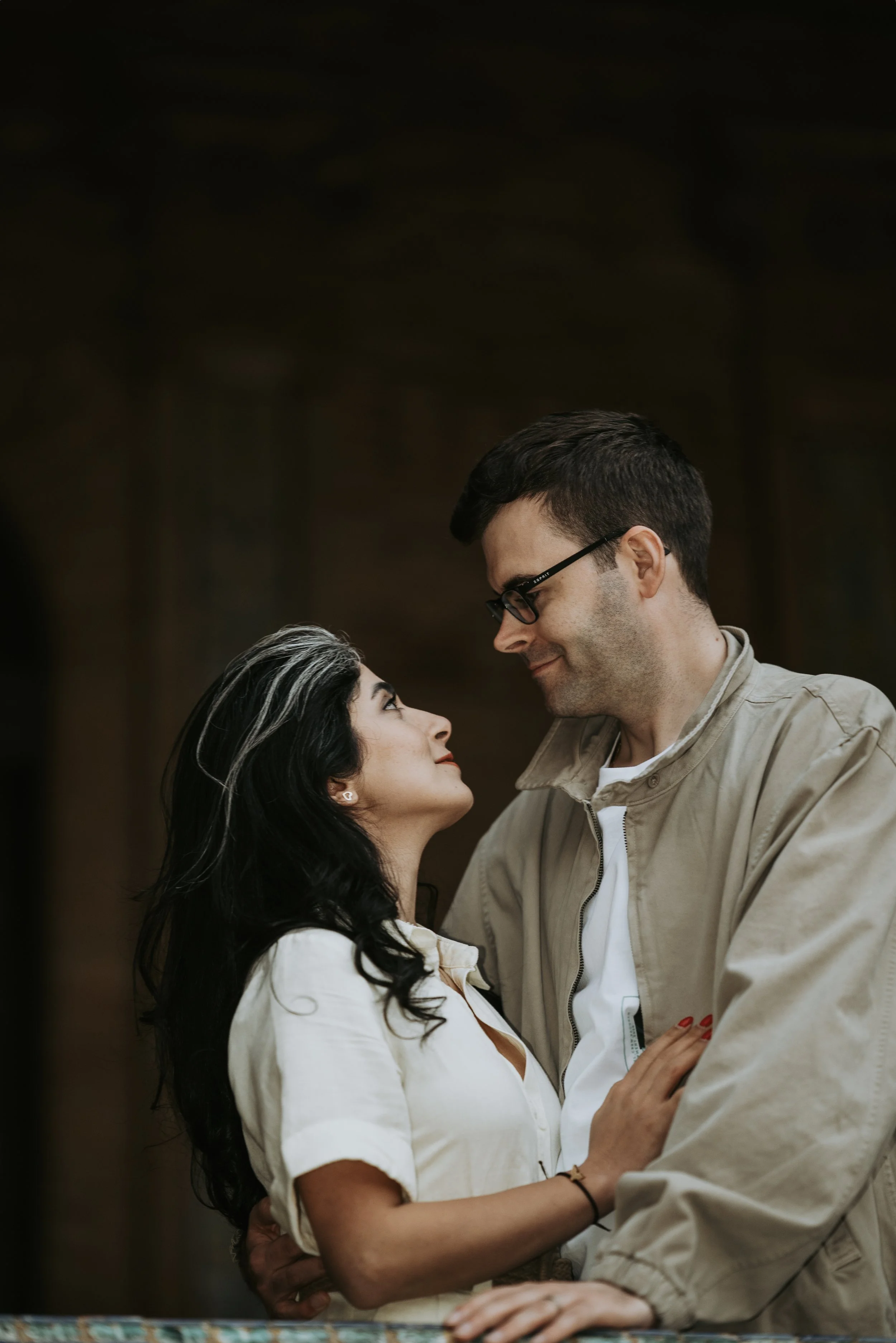 A couple gazing into each other's eyes, standing close with their arms around each other, in an intimate moment.