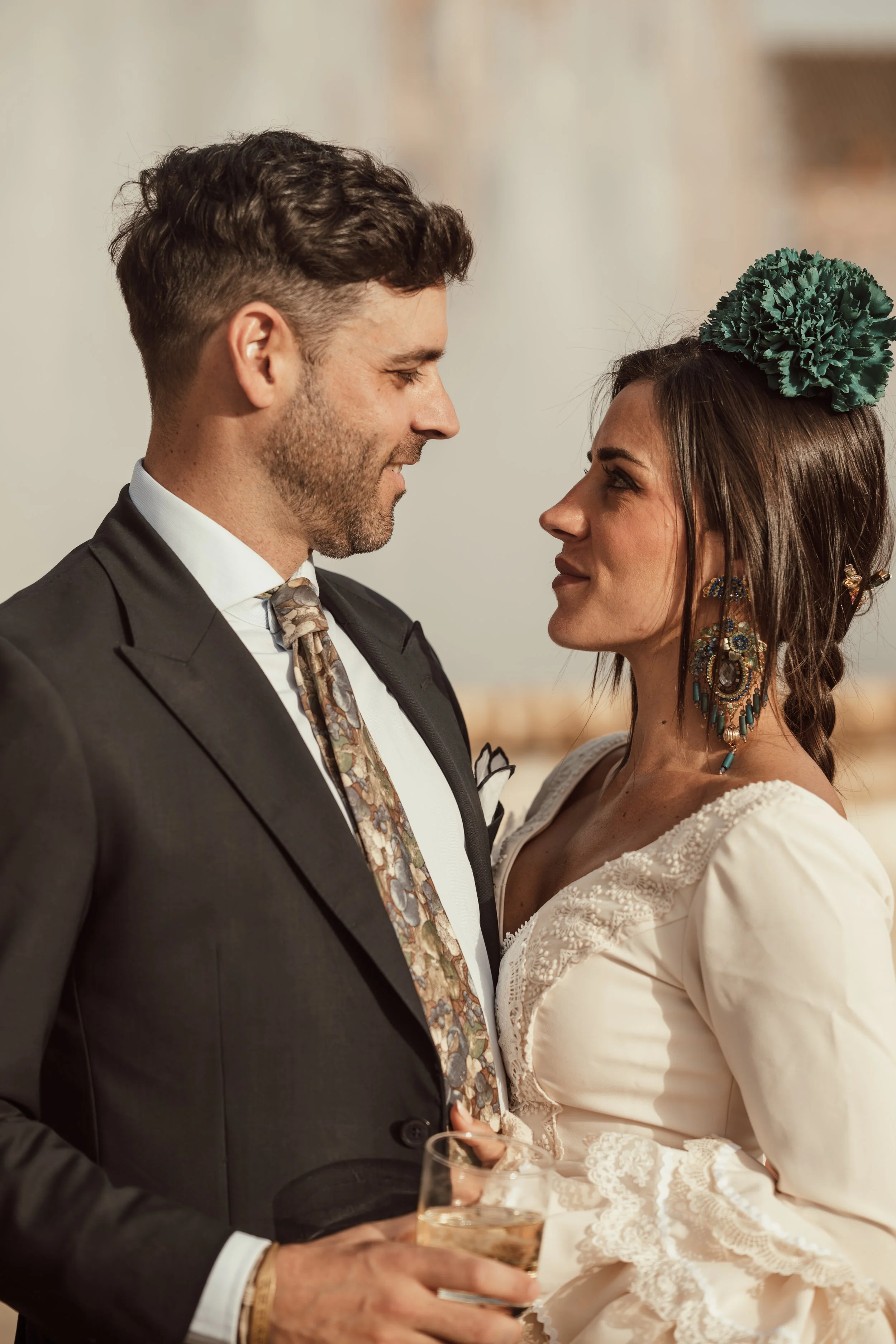 A couple in wedding attire looking at each other, with the man holding a glass of champagne and both smiling.